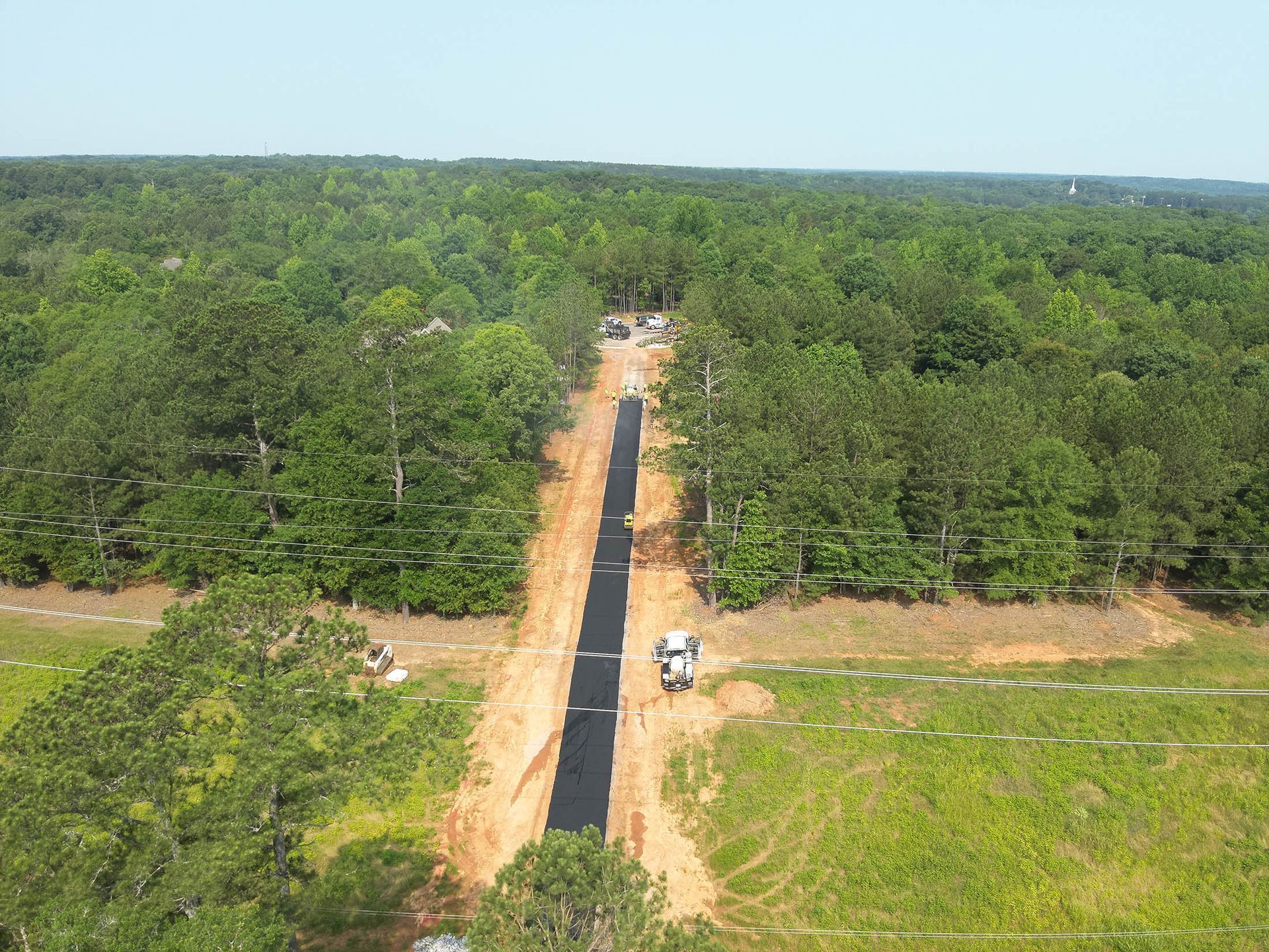 Construction site clearing trees for a long, straight path through a forest, with machinery and cleared earth visible.