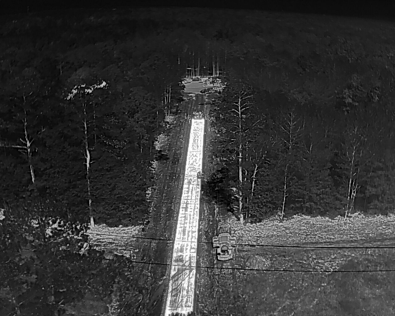 Black and white aerial view of a runway cleared through a forest, extending towards a distant clearing.