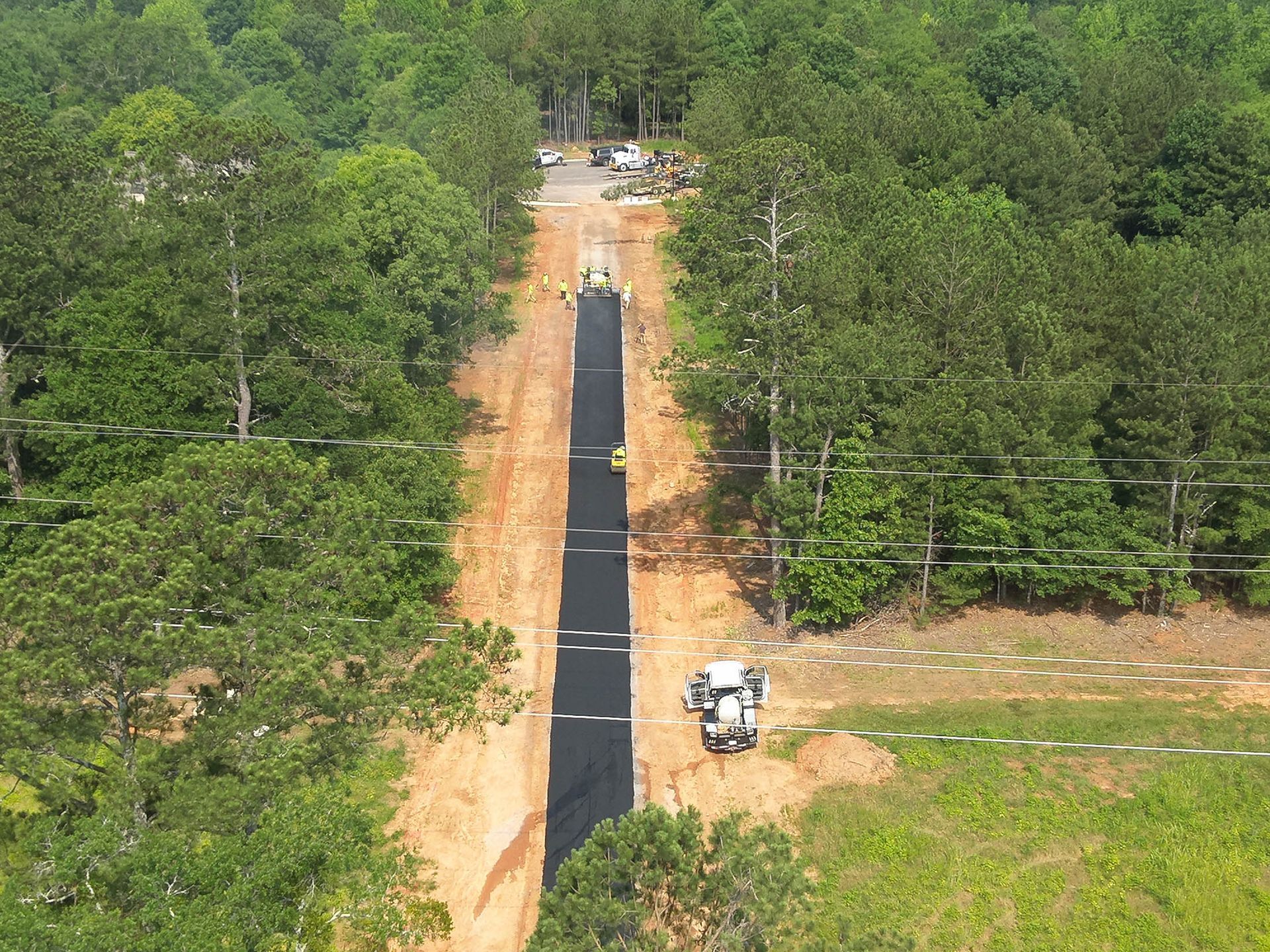 A long, narrow trench through a forest, lined with black fabric. Construction vehicles and workers are present.
