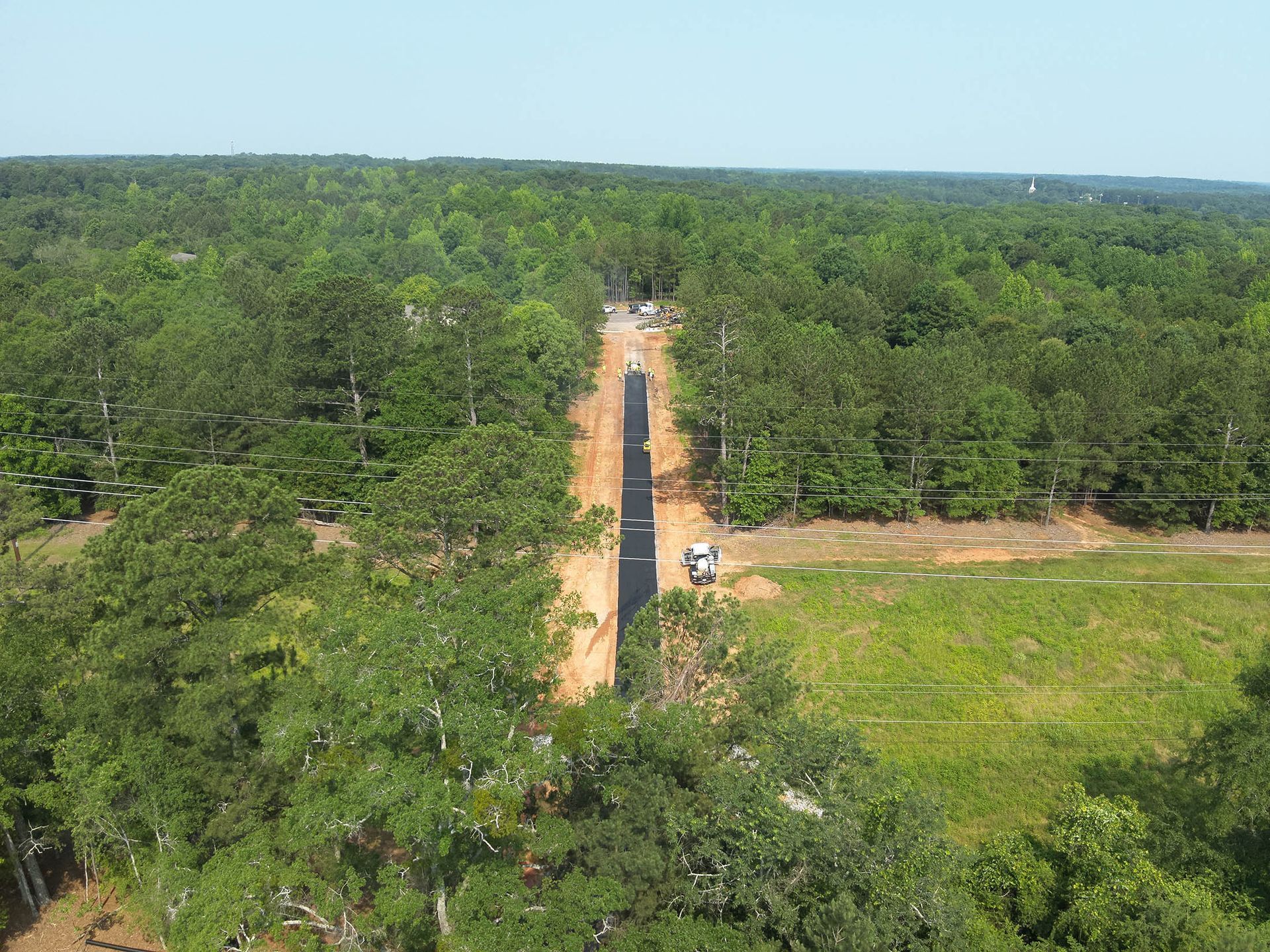 Aerial view of a dirt road cut through a dense forest, with a vehicle visible in the distance.
