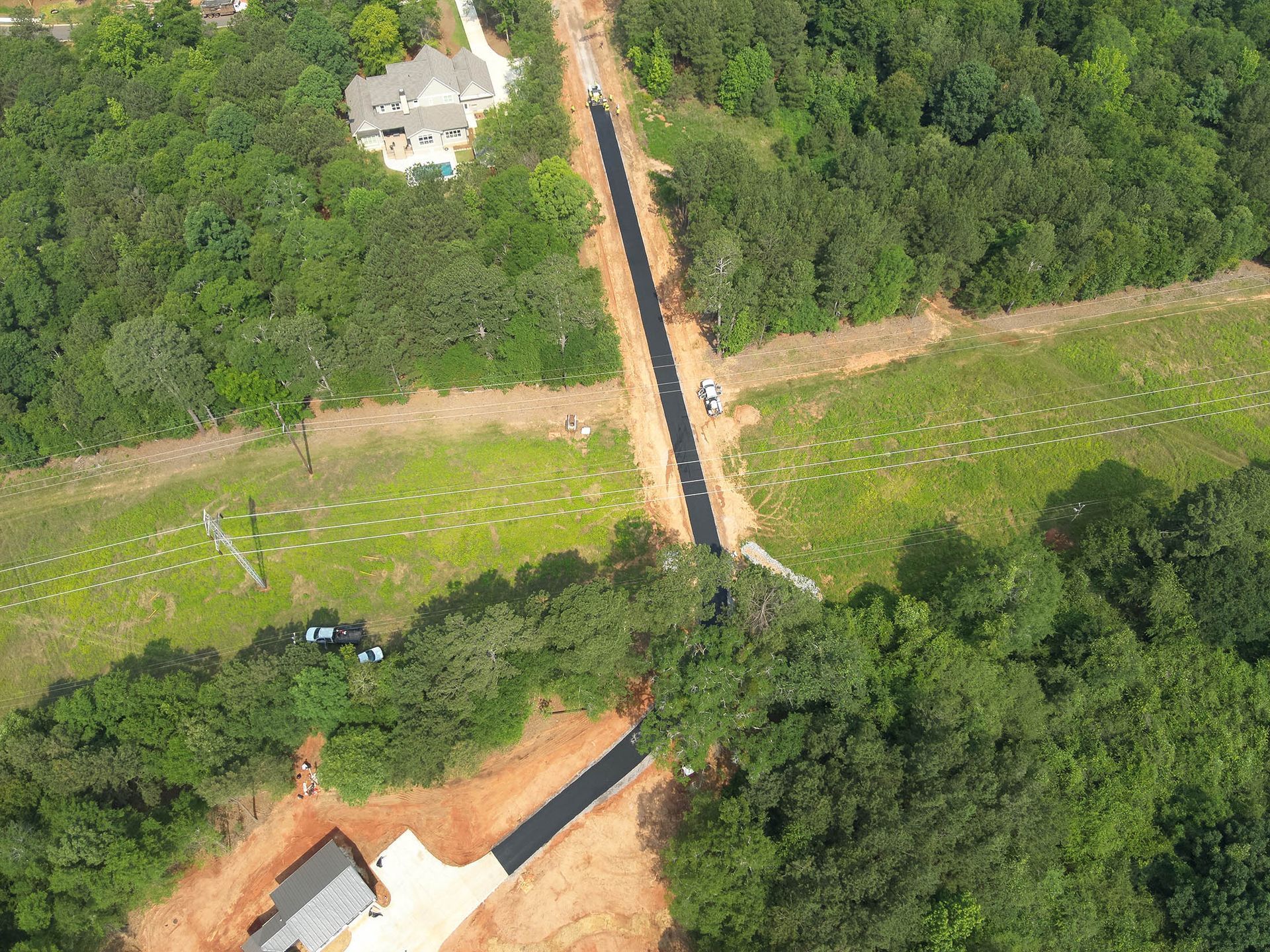 Aerial view of a clearing through a forest with asphalt pathways and scattered vegetation, and houses.