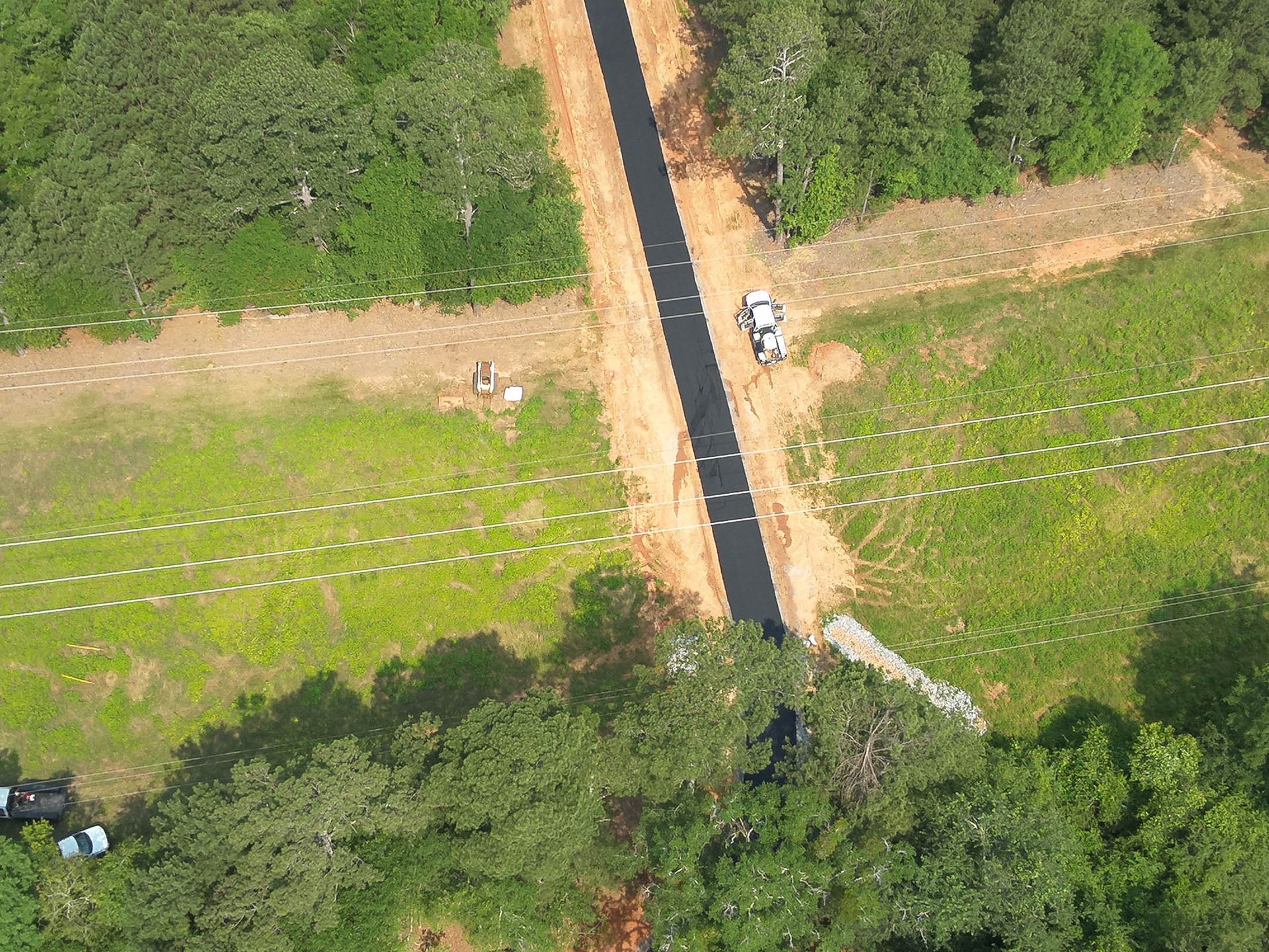 Aerial view of a paved road cutting through a grassy area and woods, with a truck on the road.