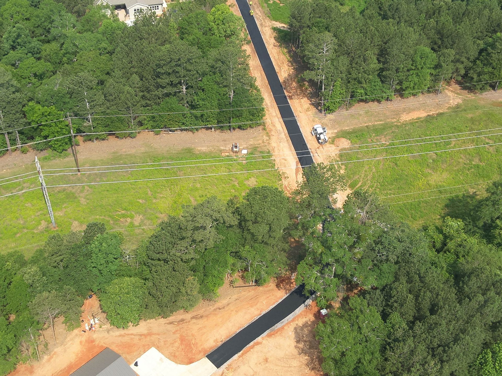 Aerial view of a paved road cutting through a wooded area. A vehicle is on the road, grass and trees surround it.