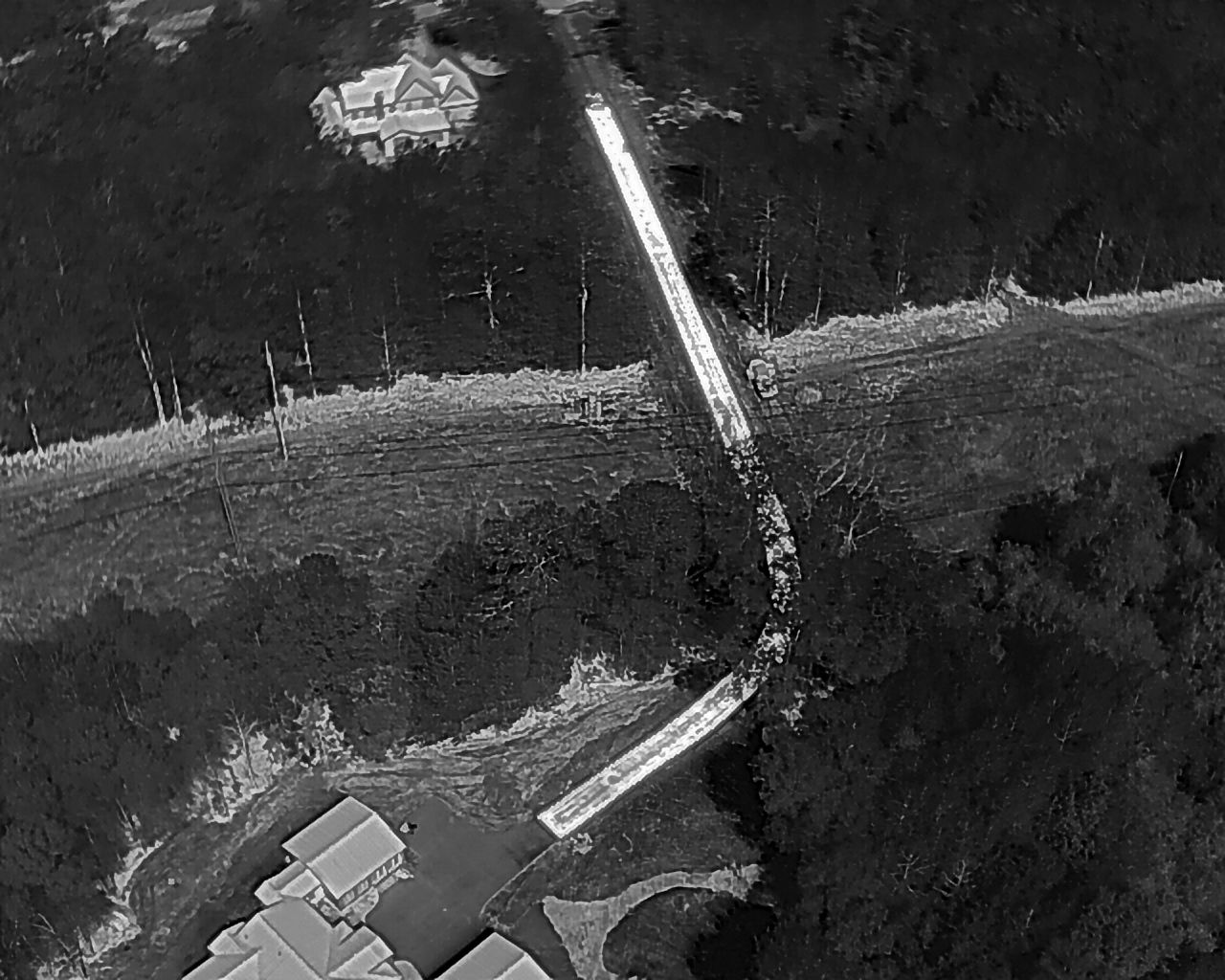 Aerial view of a road winding through a forested area, with buildings at the top and bottom.