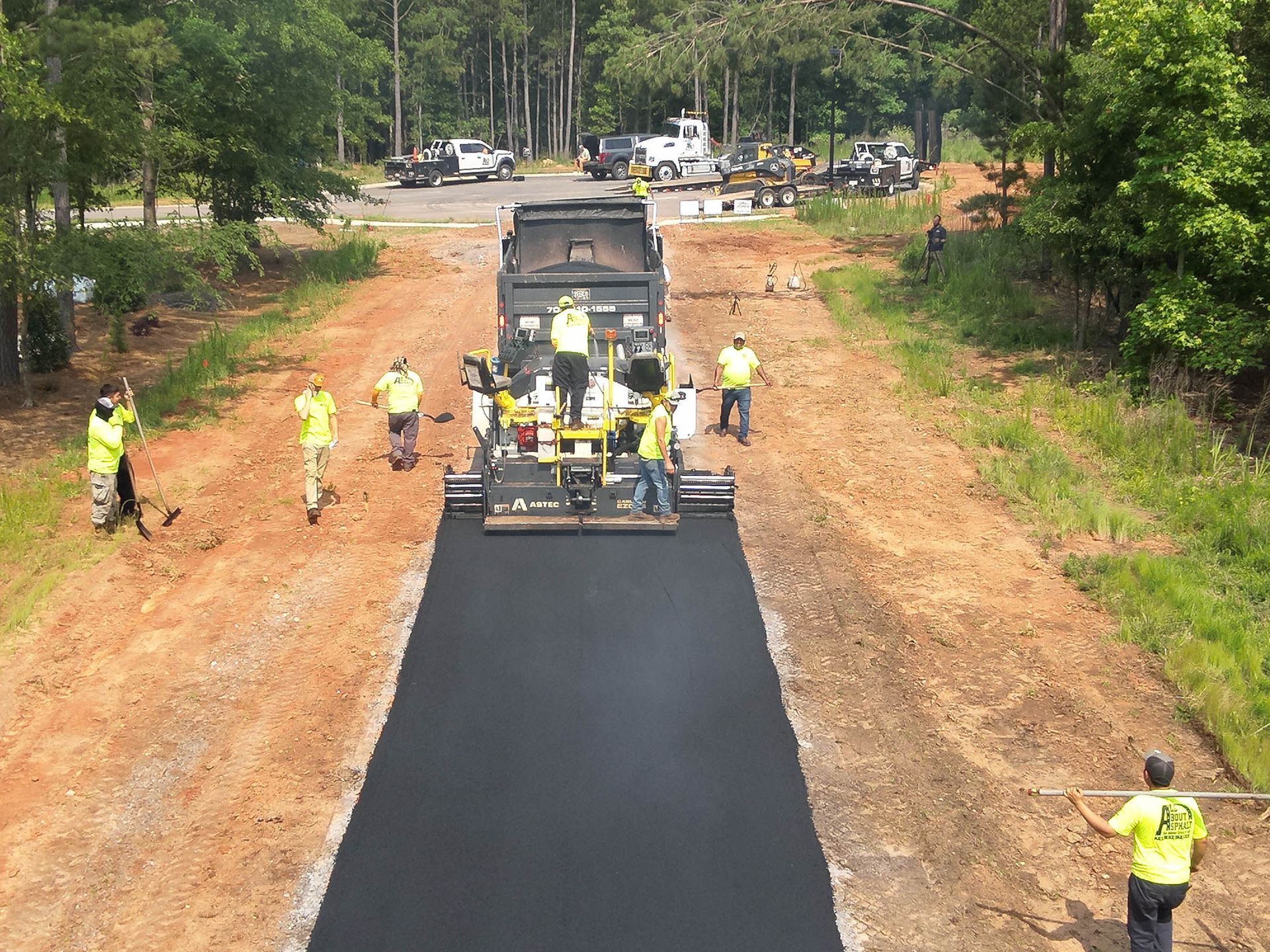 Asphalt paving crew laying asphalt on a road. Workers in safety vests surround the paver.