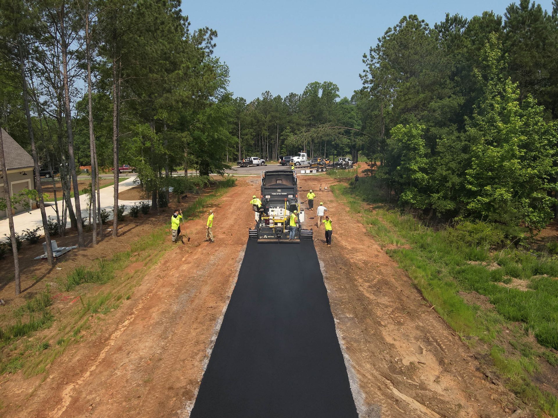 Asphalt paving in progress on a road. Workers in yellow vests operate machinery and spread asphalt.
