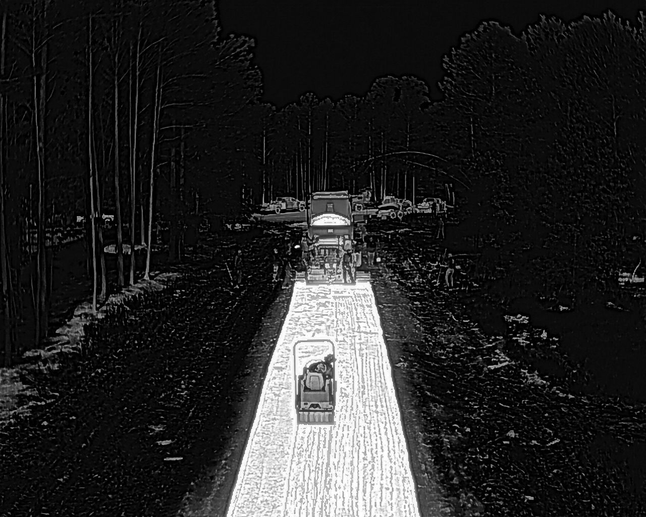 Construction equipment paving a road in a wooded area. Roller compacting asphalt.