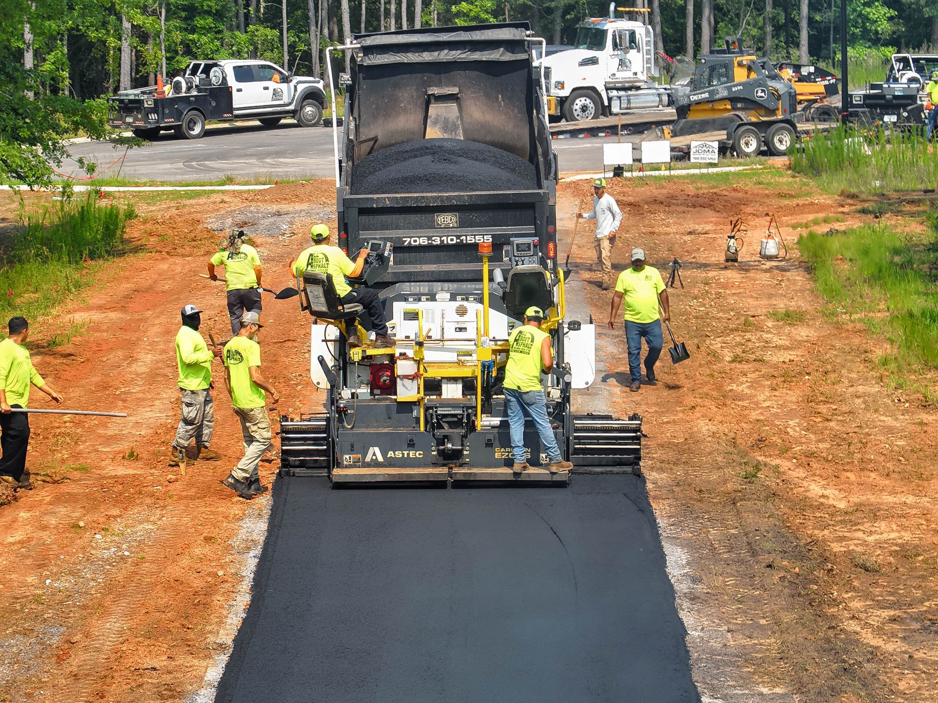 Crew in yellow vests work around a large machine, laying new asphalt on a road.