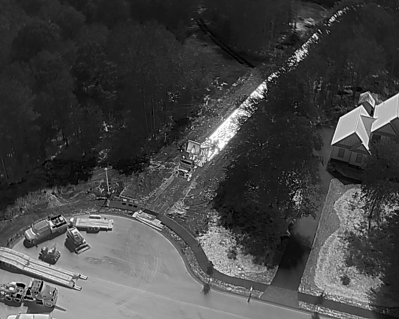 Overhead view of a forest with a stream, road, and buildings. Parked construction equipment in the foreground.