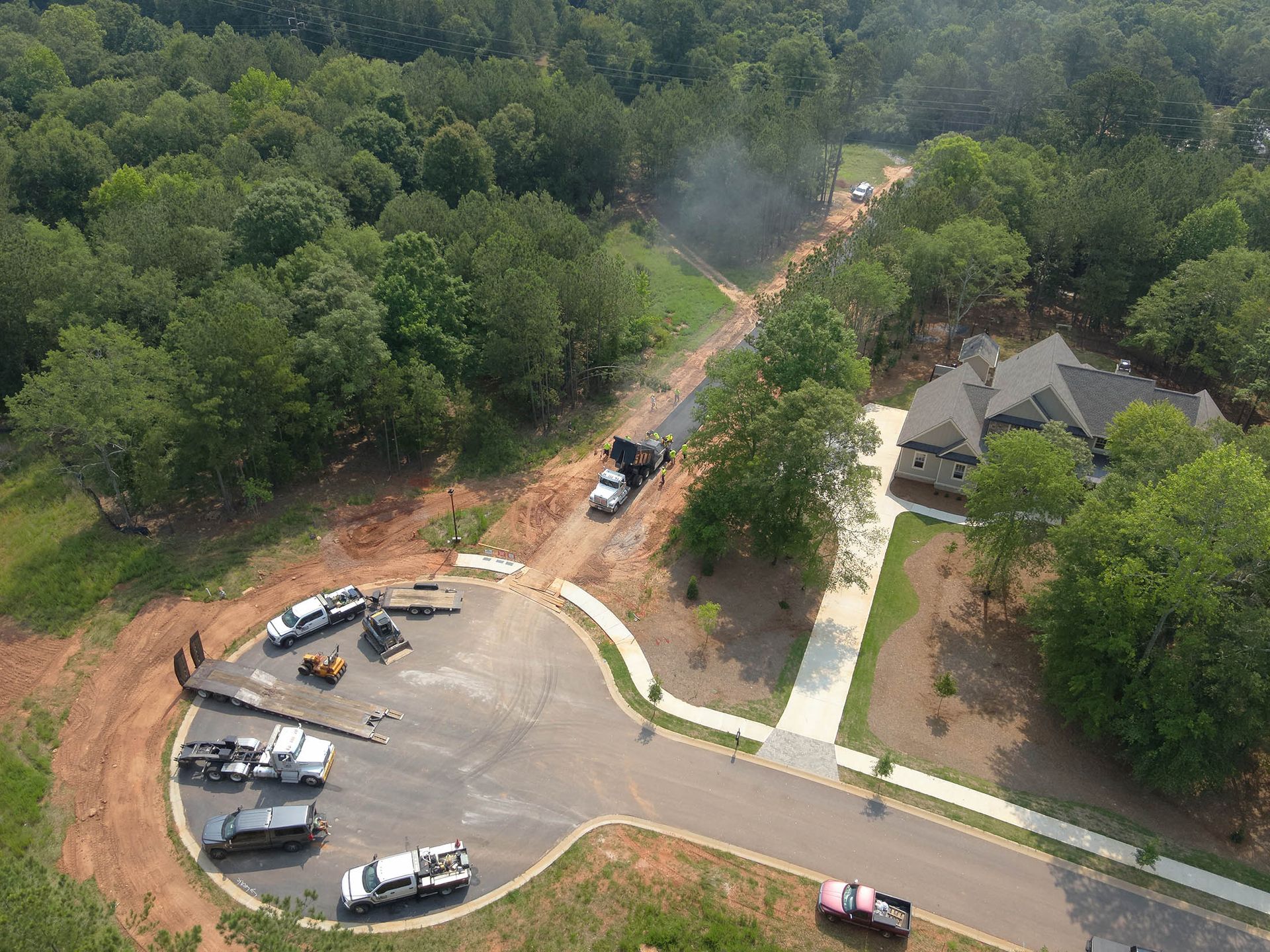 Asphalt paving construction in a residential neighborhood. Paving equipment and vehicles are visible.