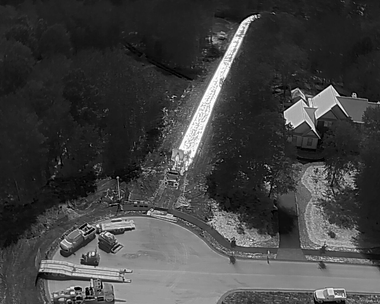 Aerial view of road construction. Heavy machinery, trees, and a house.