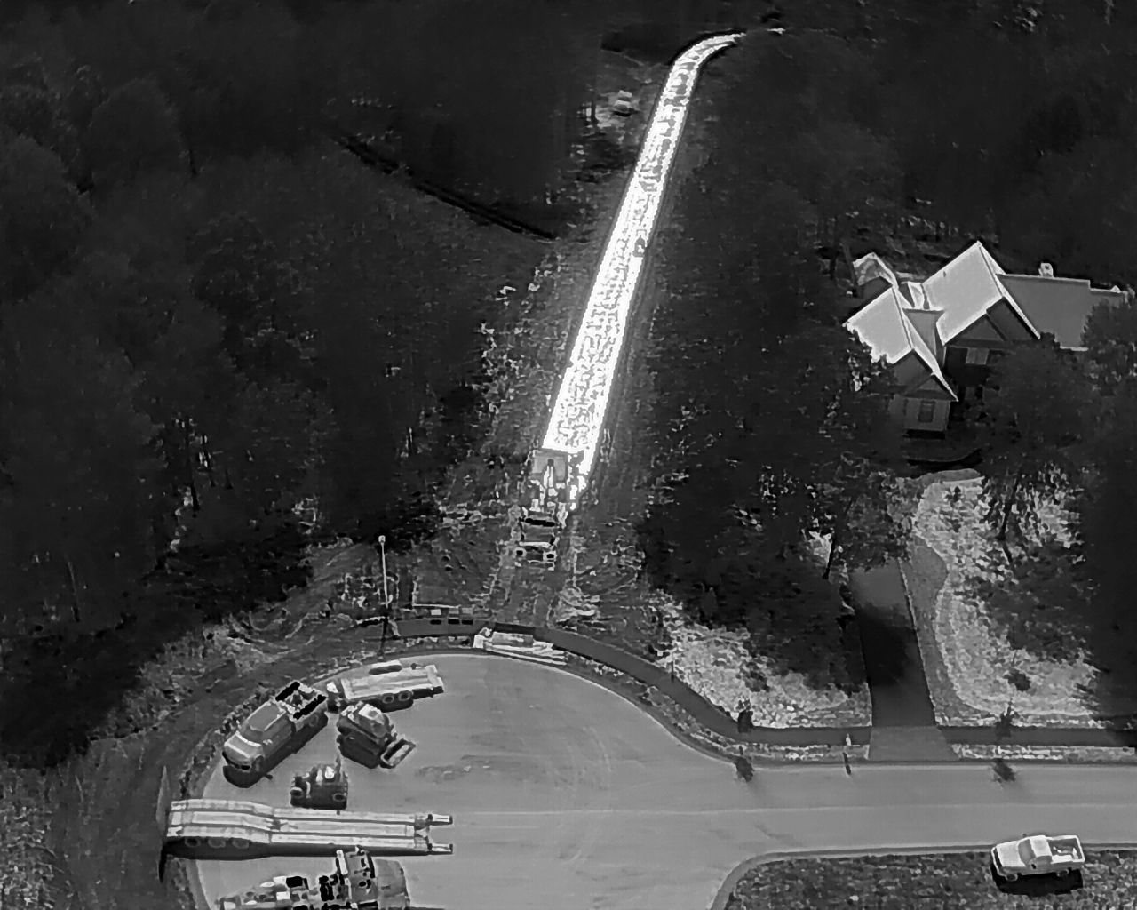 A new road is being built next to a house and dense forest, with construction equipment visible.