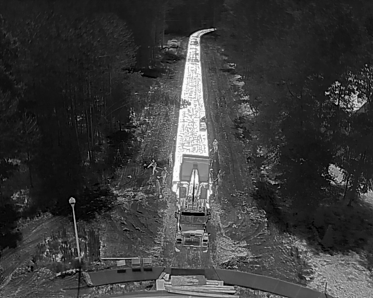 Aerial view of a long, paved path through a forest, leading to a bridge with a vehicle parked on it.
