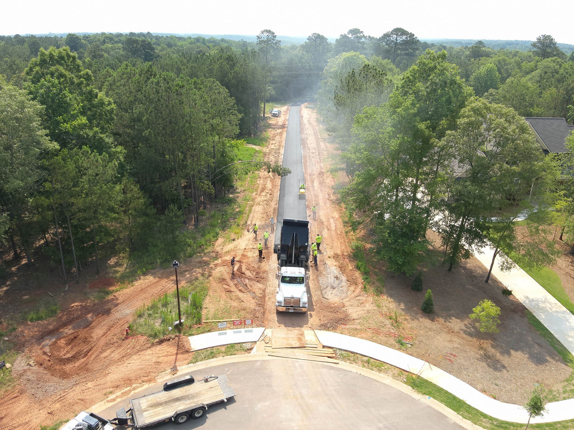 Asphalt being poured from a truck on a tree-lined road.