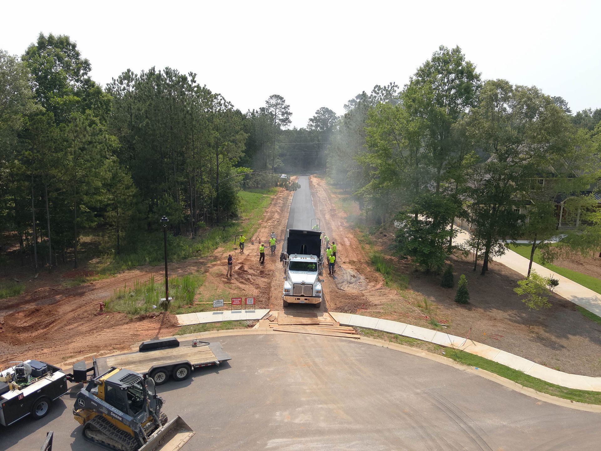 A semi-truck unloading asphalt on a newly paved road, with construction workers nearby.