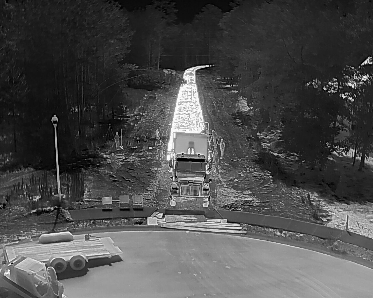 A ski jumping ramp at night, illuminated by lights, slopes upward through a wooded area.