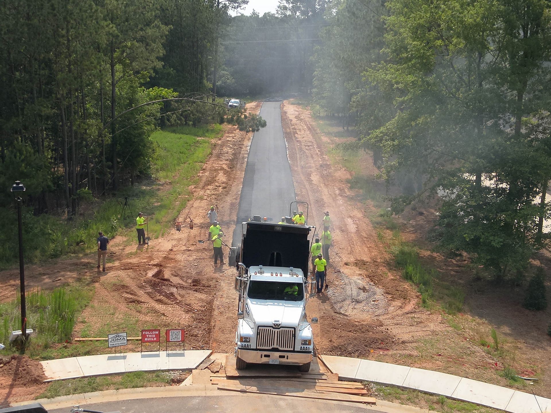 Dump truck depositing asphalt on new road surface, workers in vests.