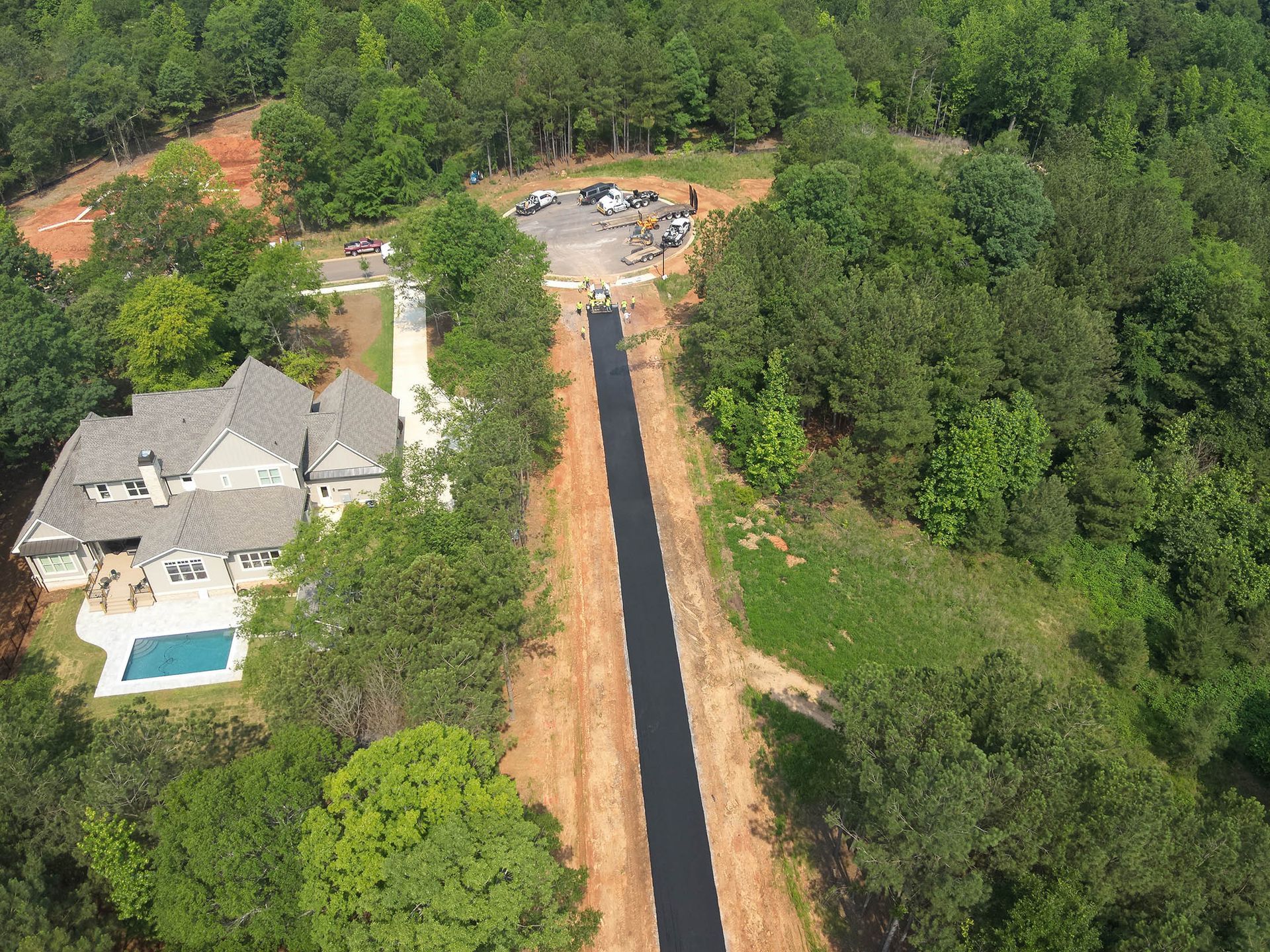 Aerial view of a home with a long driveway and pool surrounded by lush green trees.