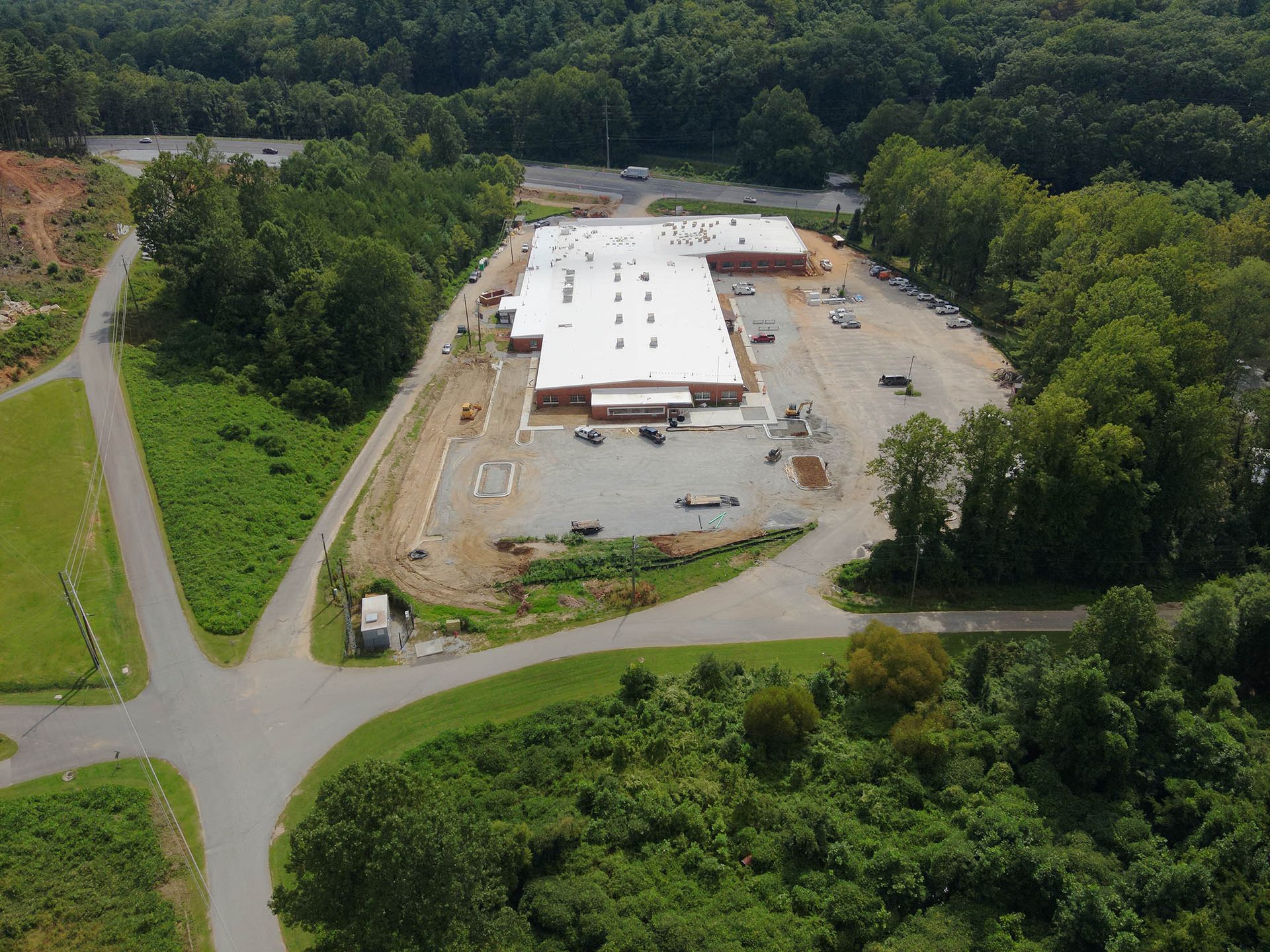 Aerial view of a building under construction, surrounded by trees and a dirt lot.