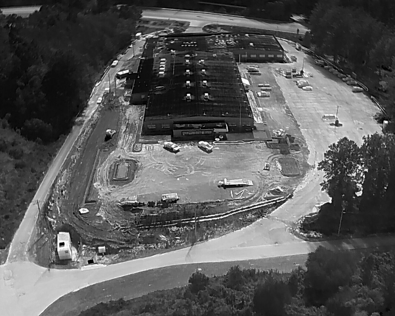 Aerial view of a large building complex with a flat roof, surrounded by a parking lot and construction activity.
