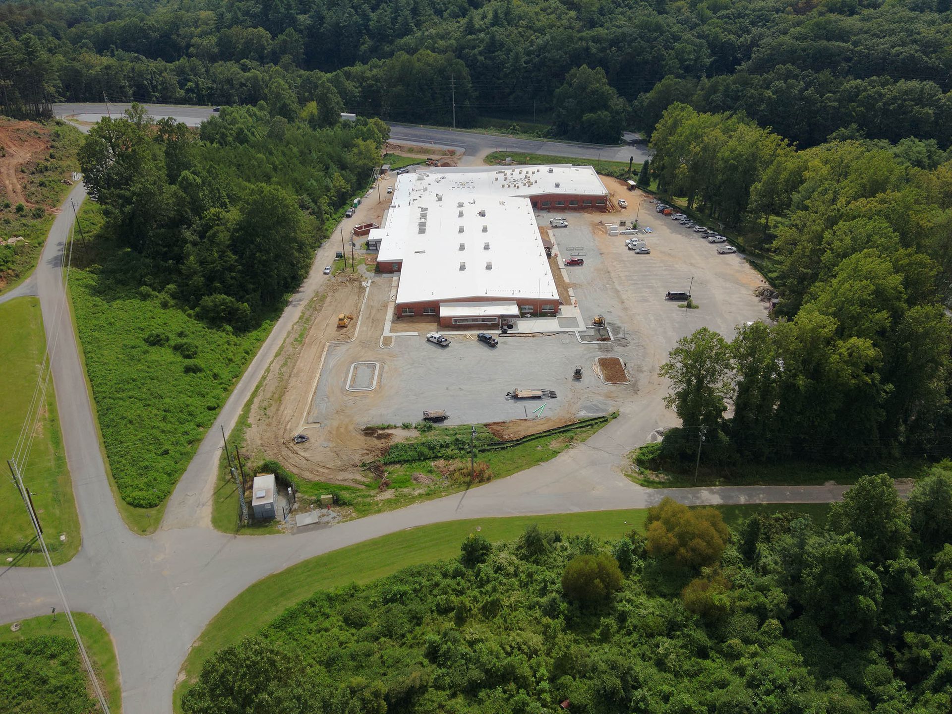 Aerial view of a large commercial building under construction surrounded by trees and a parking lot.