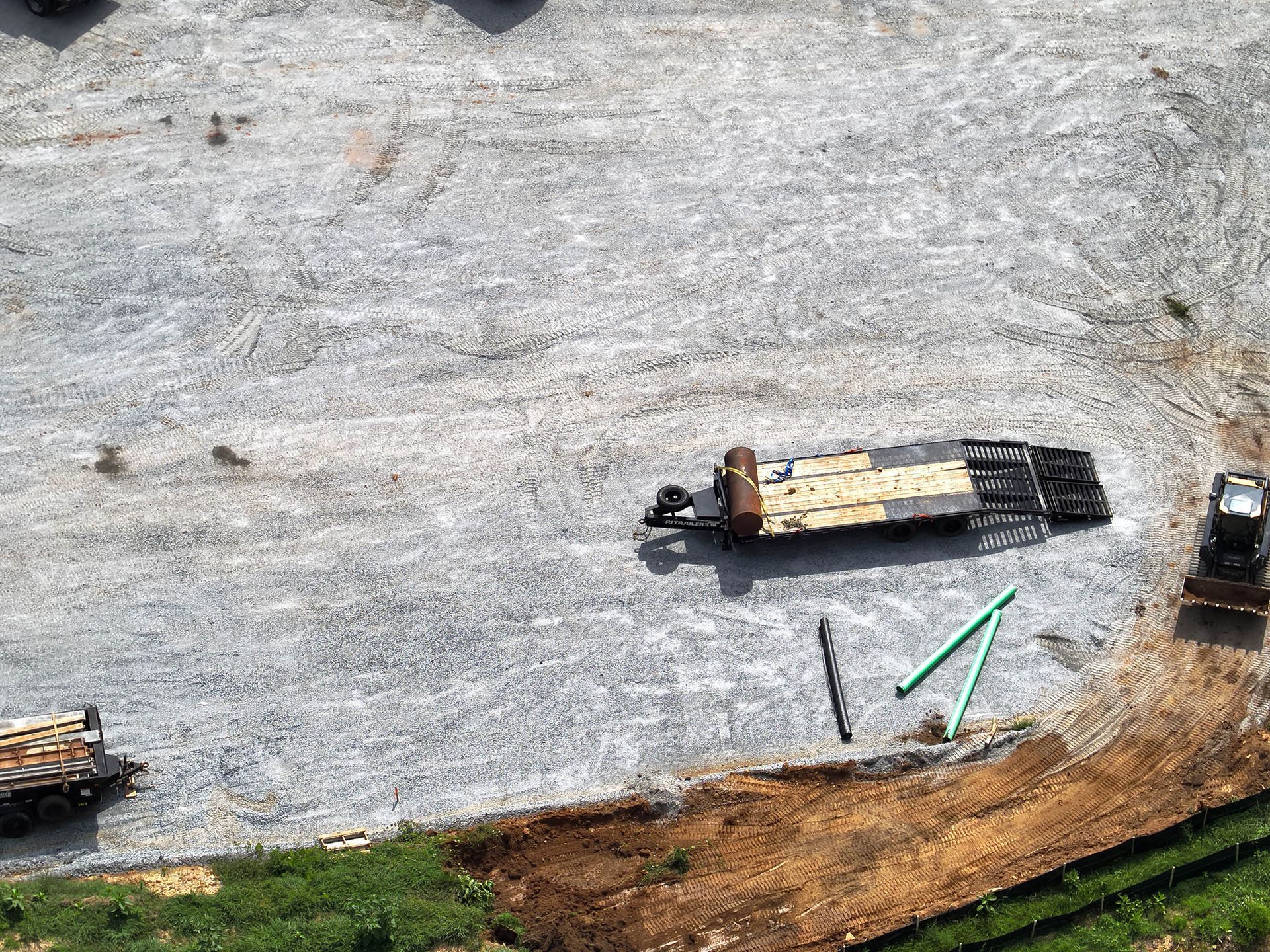 Gravel lot with two trailers loaded with wood.  Pipes and earthwork at the edge.