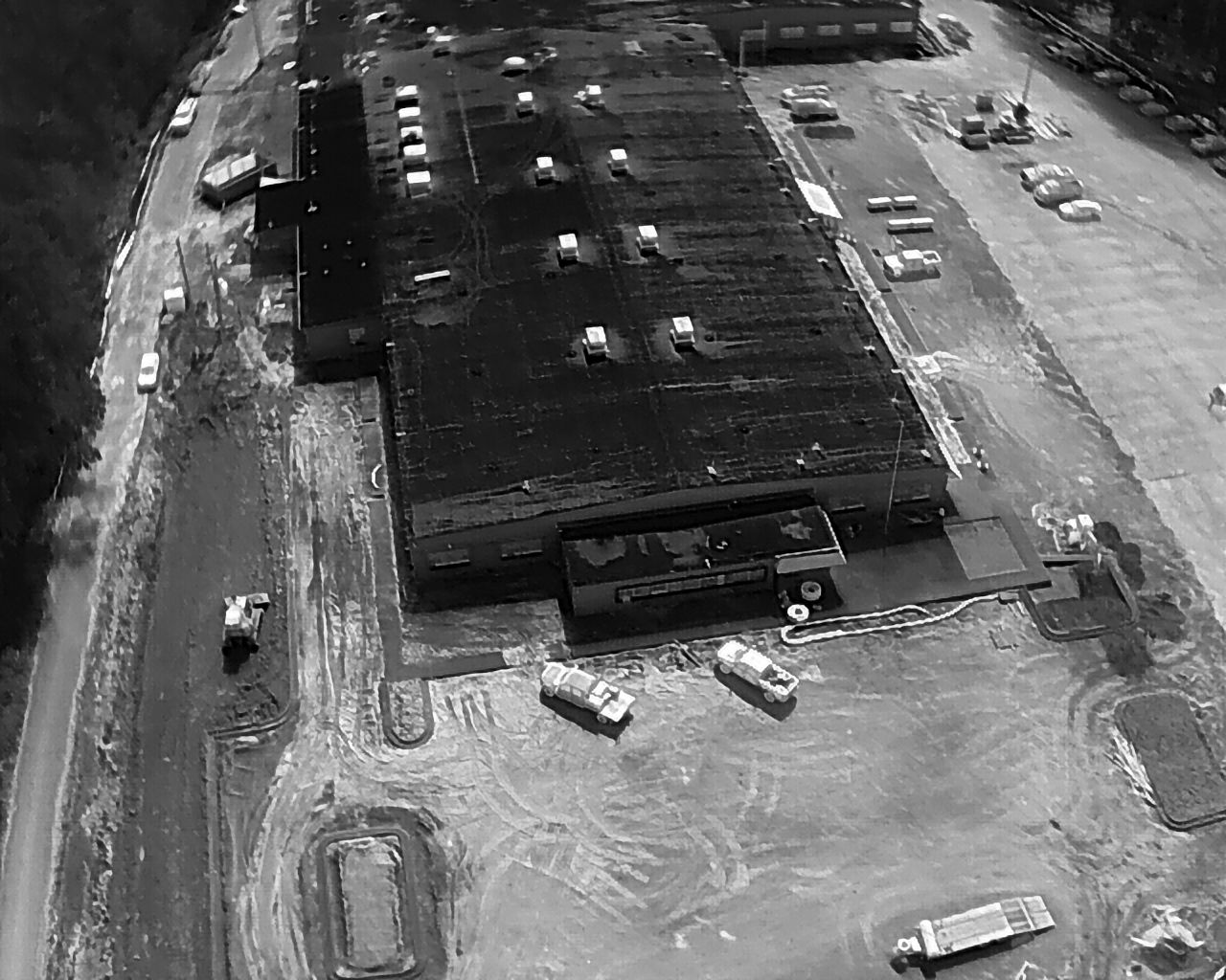 Aerial view of a large building with a flat roof, surrounded by a parking lot and a road.