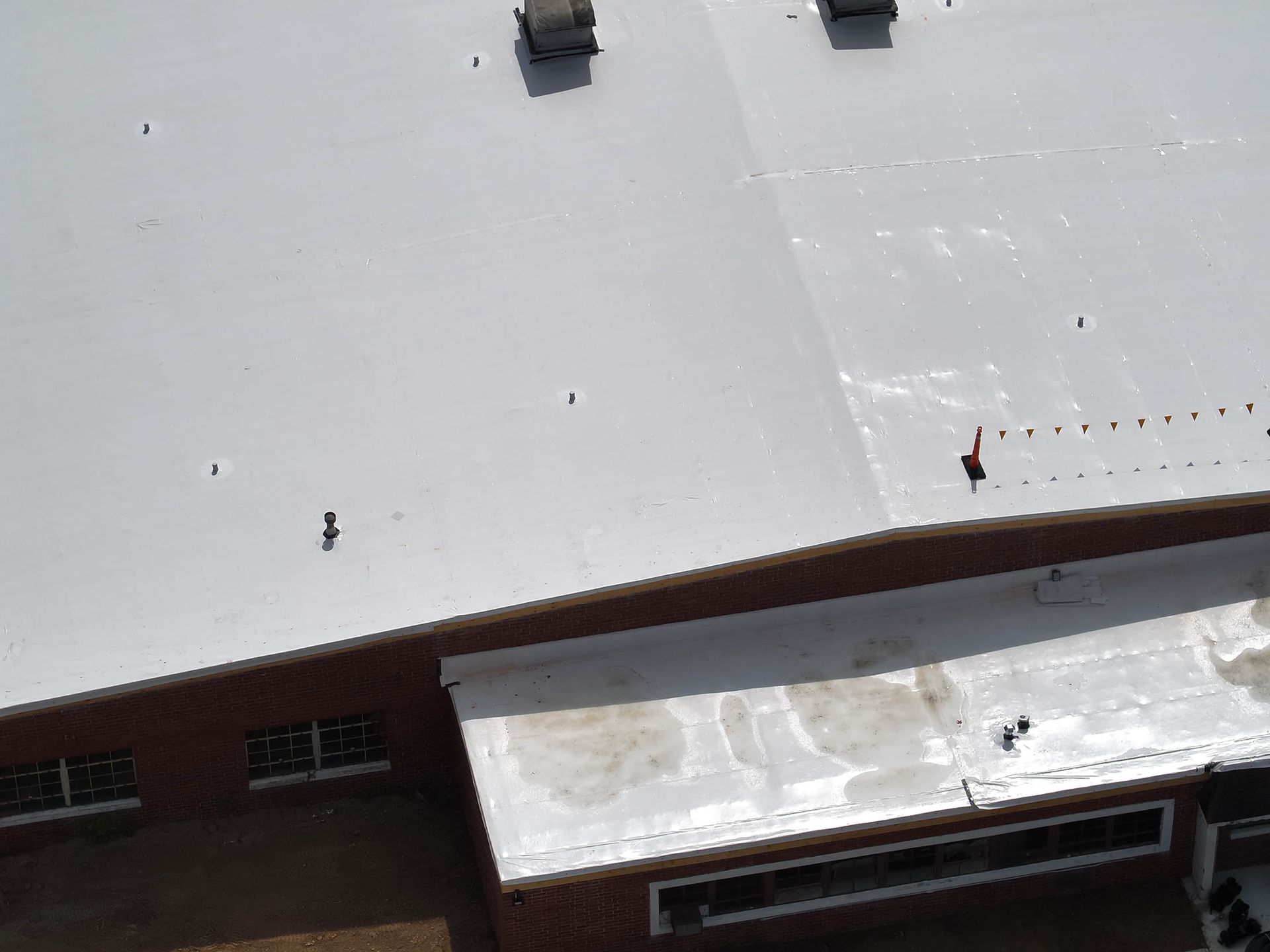 White commercial building roof with vents, over a red brick wall.