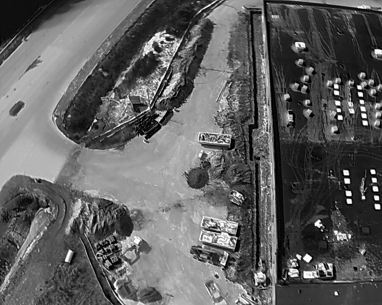 Aerial view of a coastal area with water, land, and structures. Includes boats, buildings, and a long barrier.