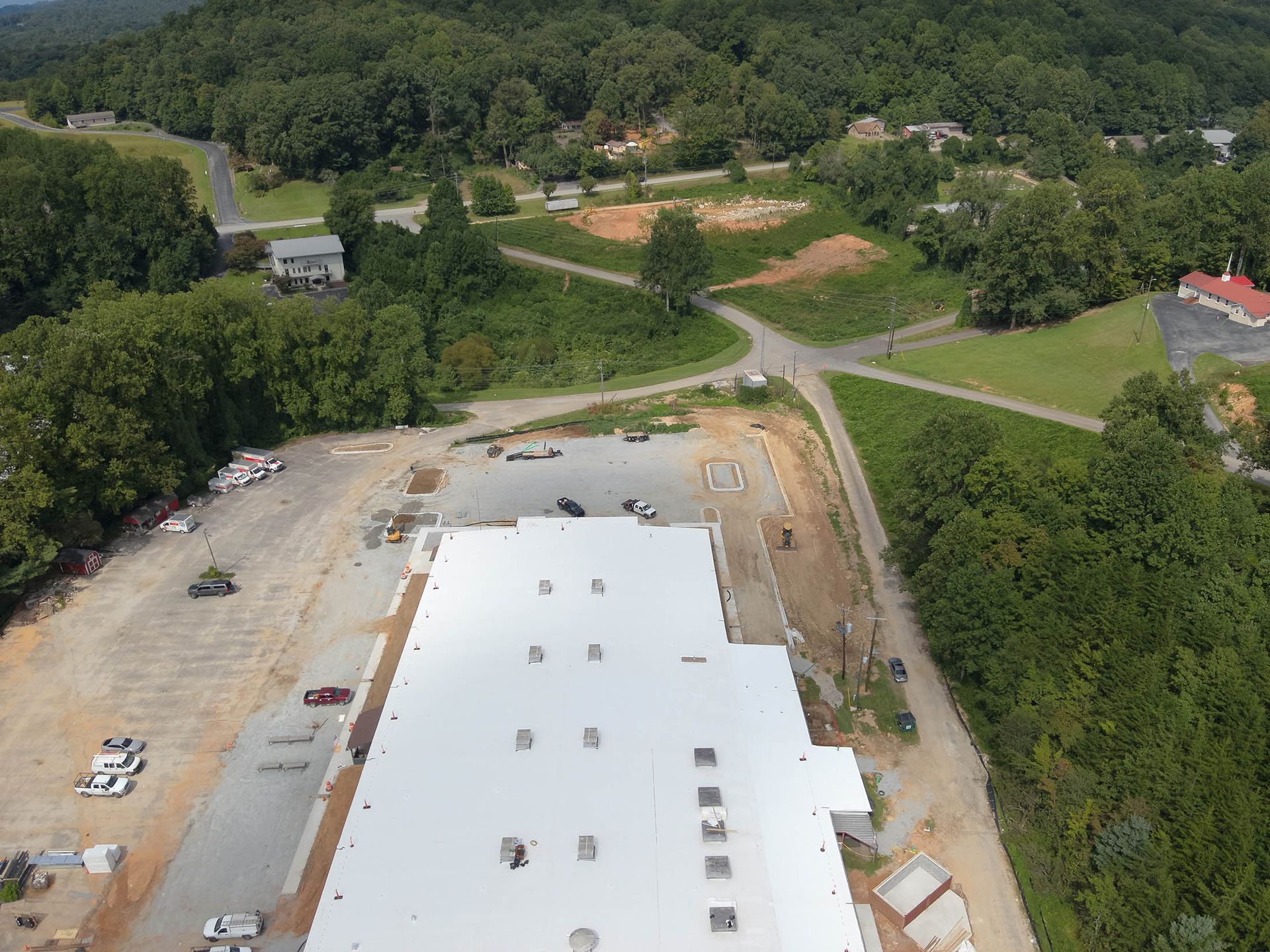Aerial view of a large building with a white roof, surrounded by a parking lot and trees.