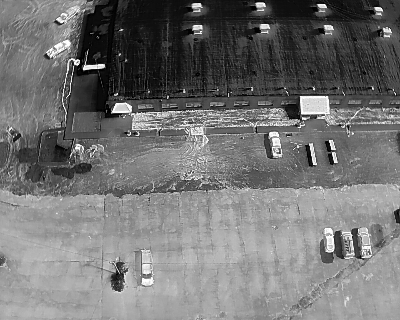 Aerial view of a flooded building and parking lot with several cars and boats.