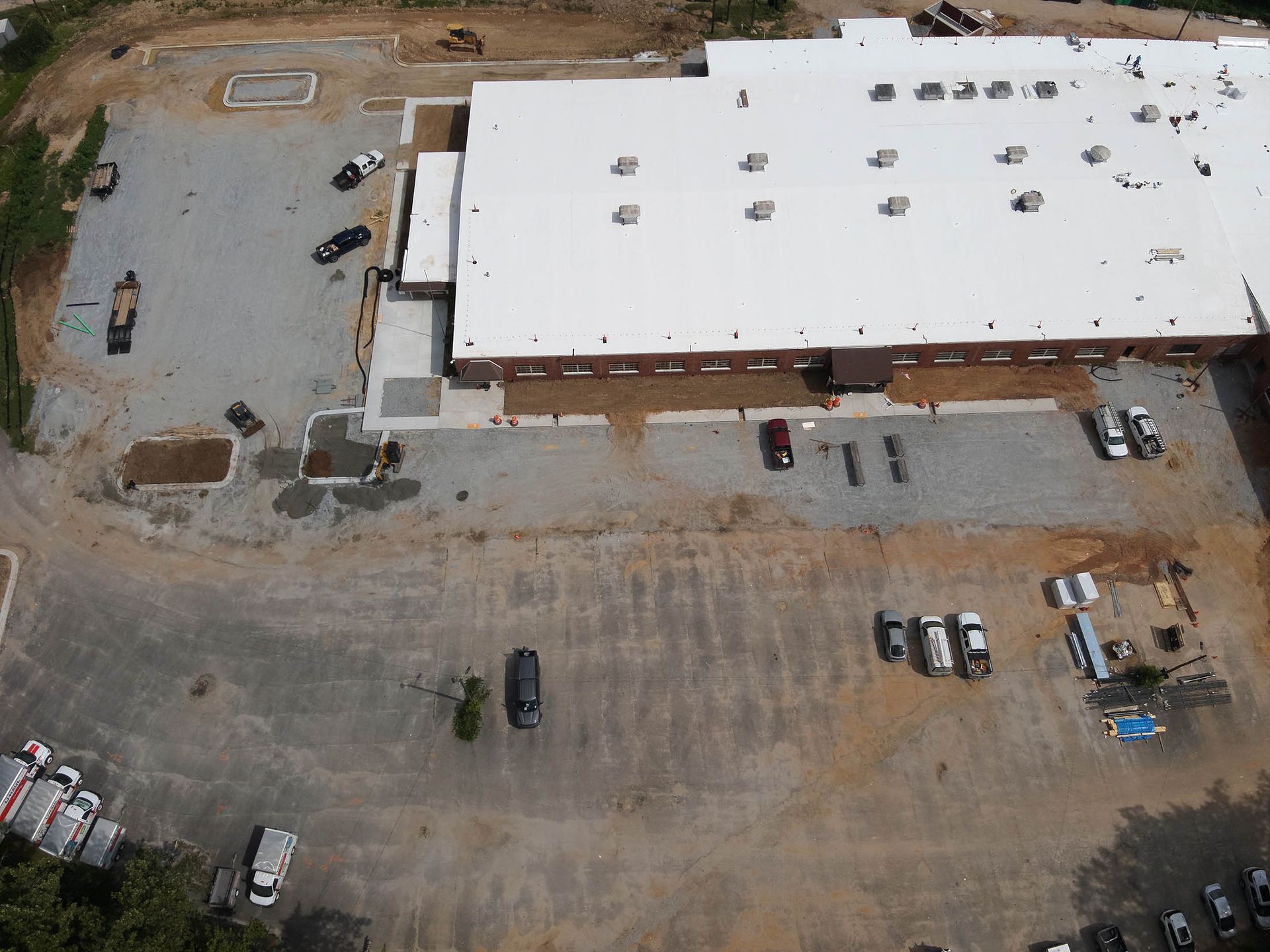 Aerial view of a commercial building with white roof, parking area, and construction activity.