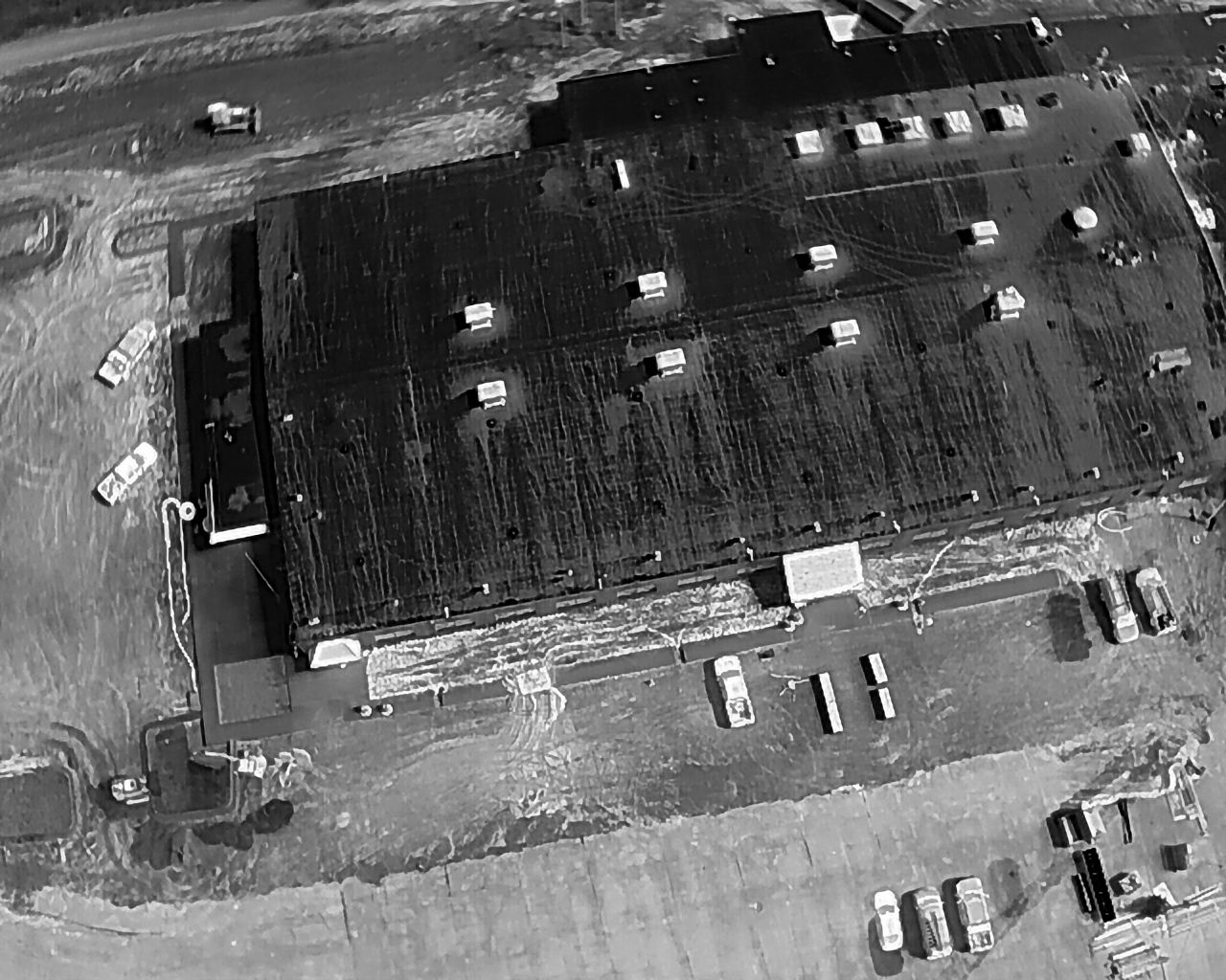 Aerial view of a flooded building with parked vehicles nearby. Gray and black tones.