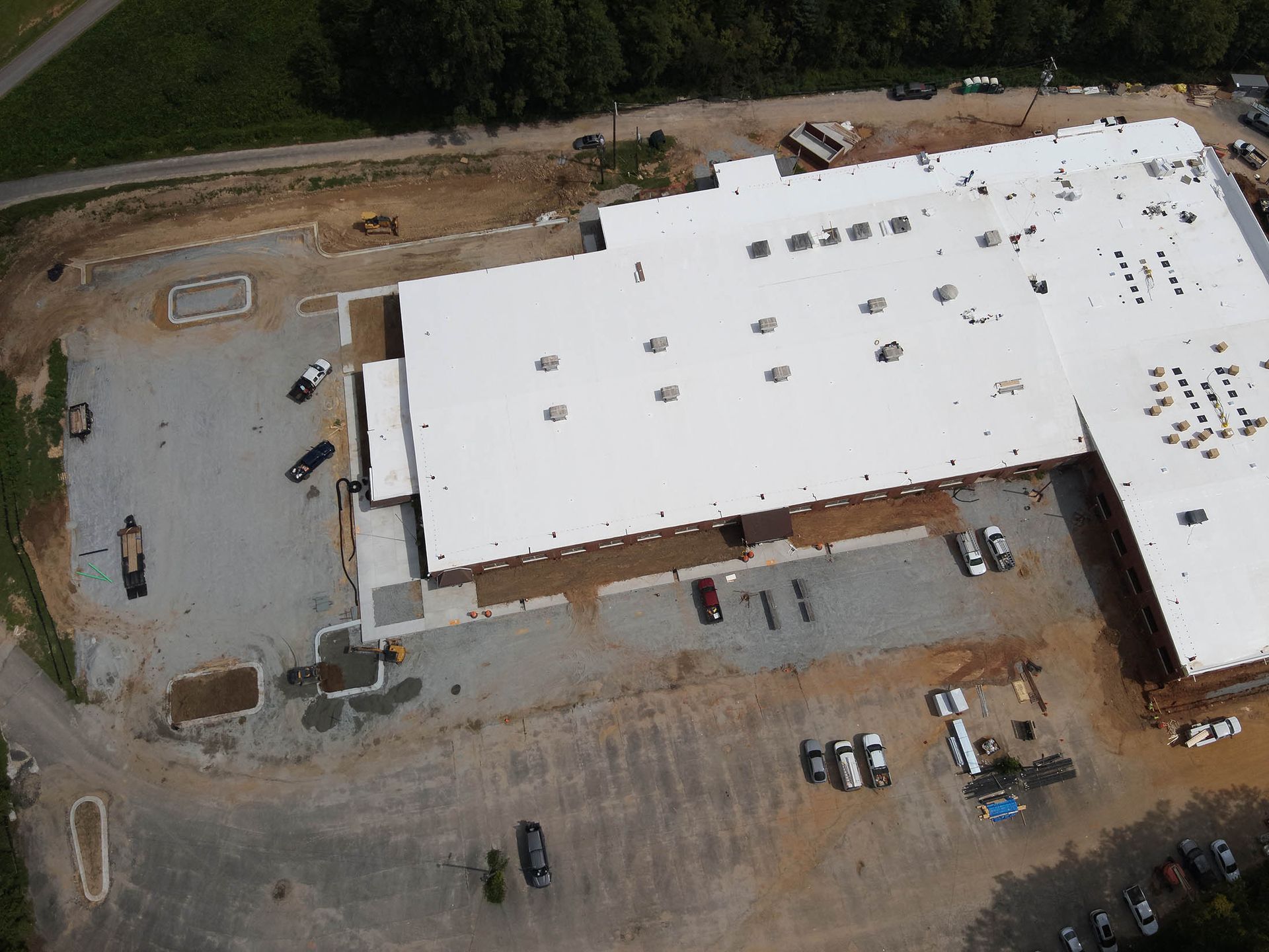 Aerial view of a large white-roofed building under construction. Vehicles and equipment scattered around.