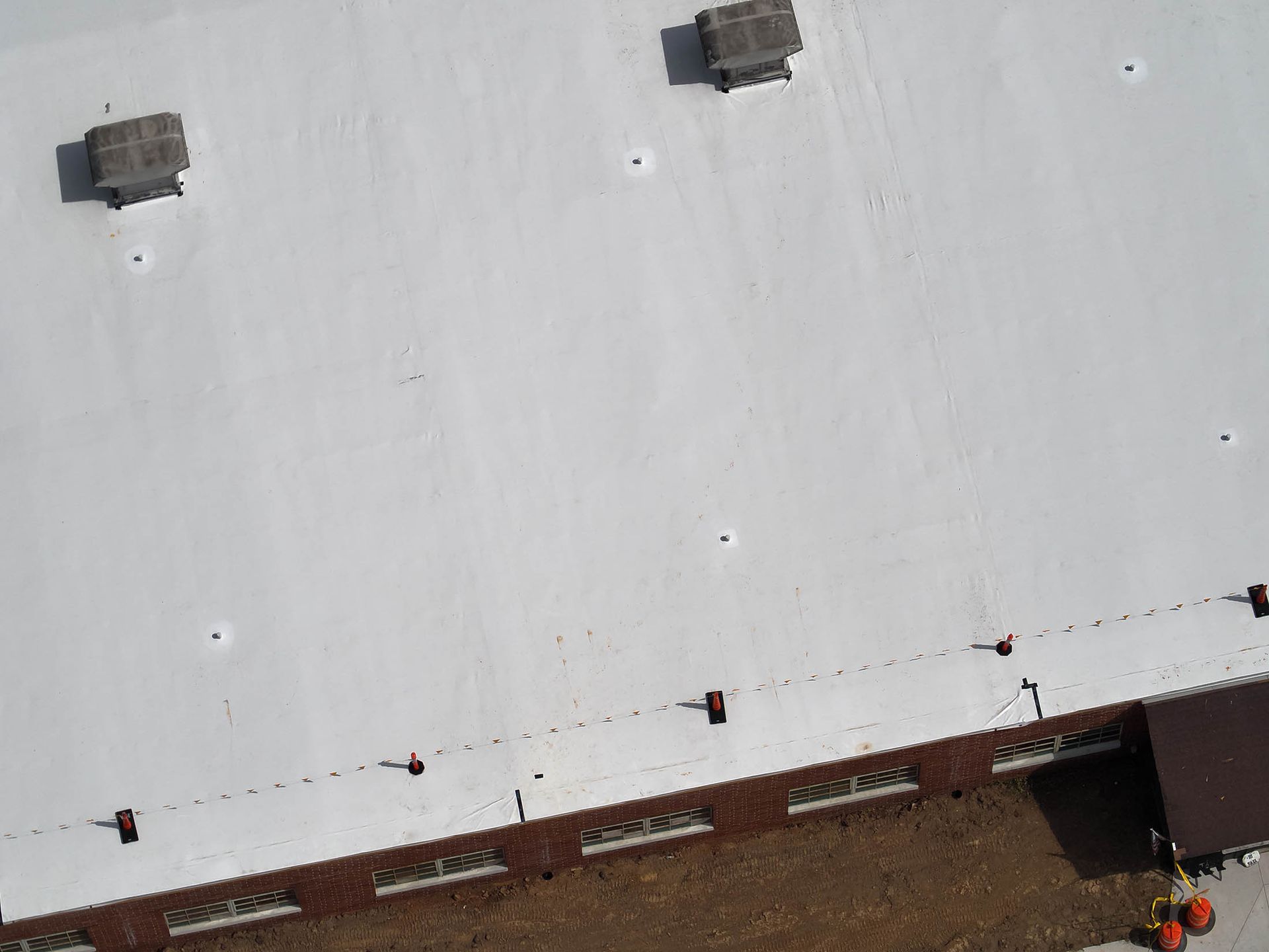 Aerial view of a white commercial roof with two vents and a brick building facade.