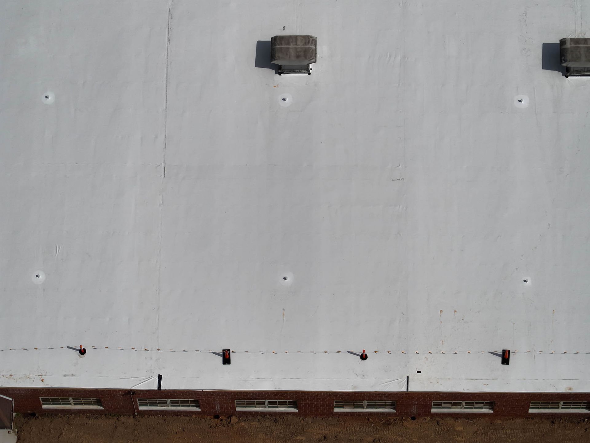 Overhead view of a white painted building roof with ventilation units and a brown brick wall with windows at the base.
