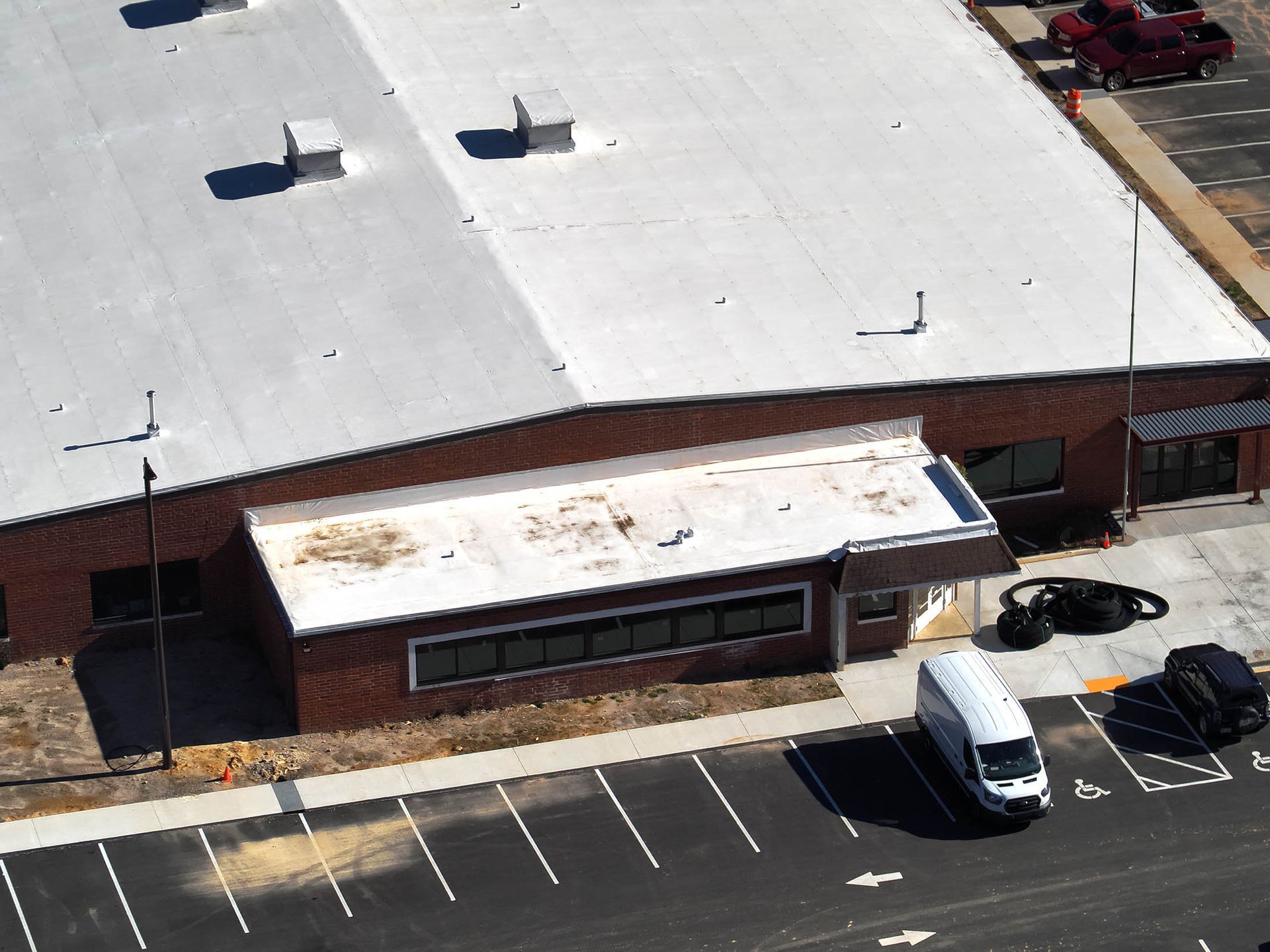Building with white roof, red brick walls, and a parking lot with a white van.