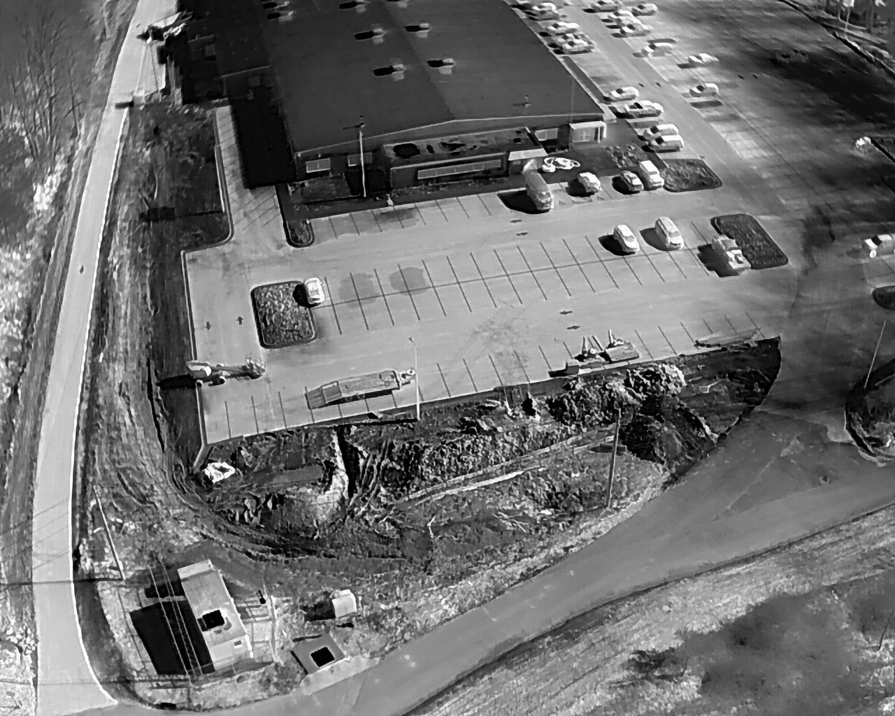 Overhead view of a commercial building with a large parking lot and surrounding land.