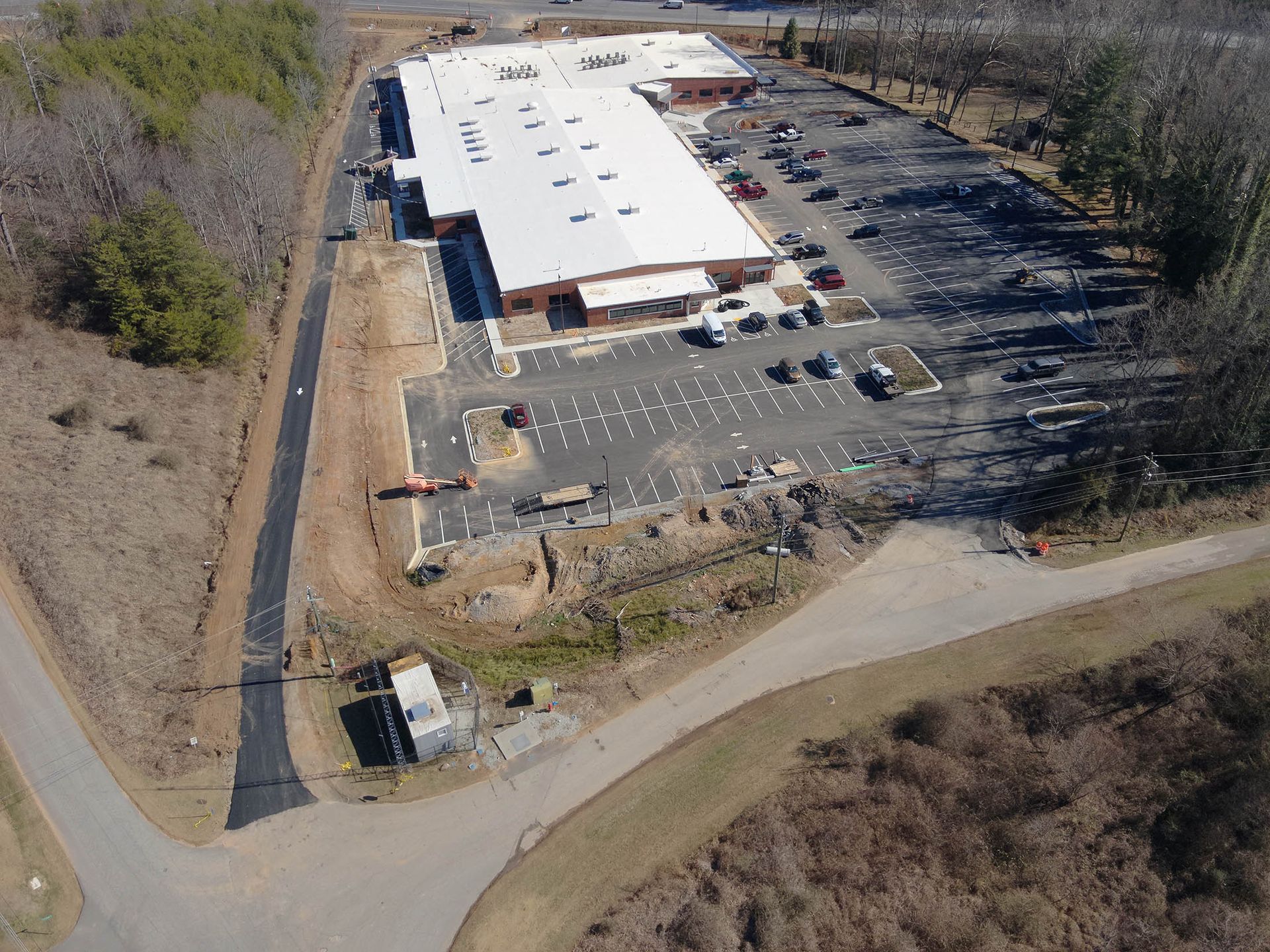 Aerial view of a long, white-roofed industrial building with parking and access roads.