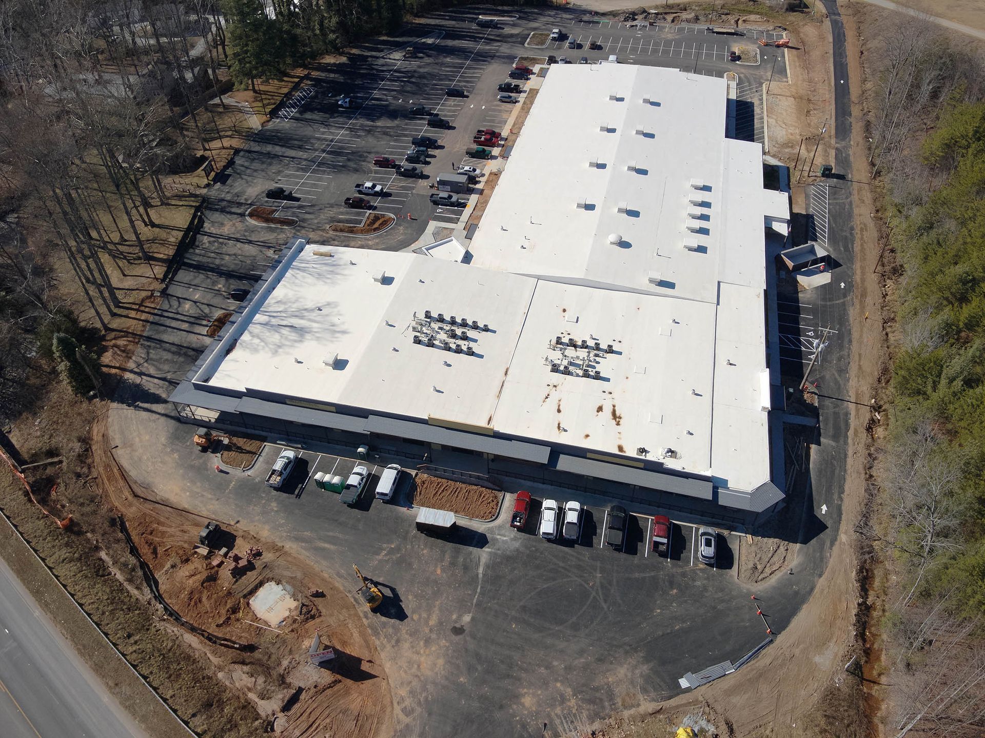 Aerial view of a large white commercial building with a parking lot and surrounding trees.