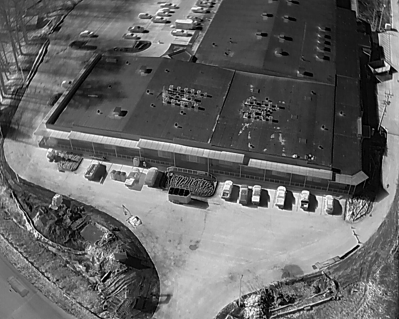 Overhead view of a commercial building with a dark roof and a parking lot filled with vehicles.