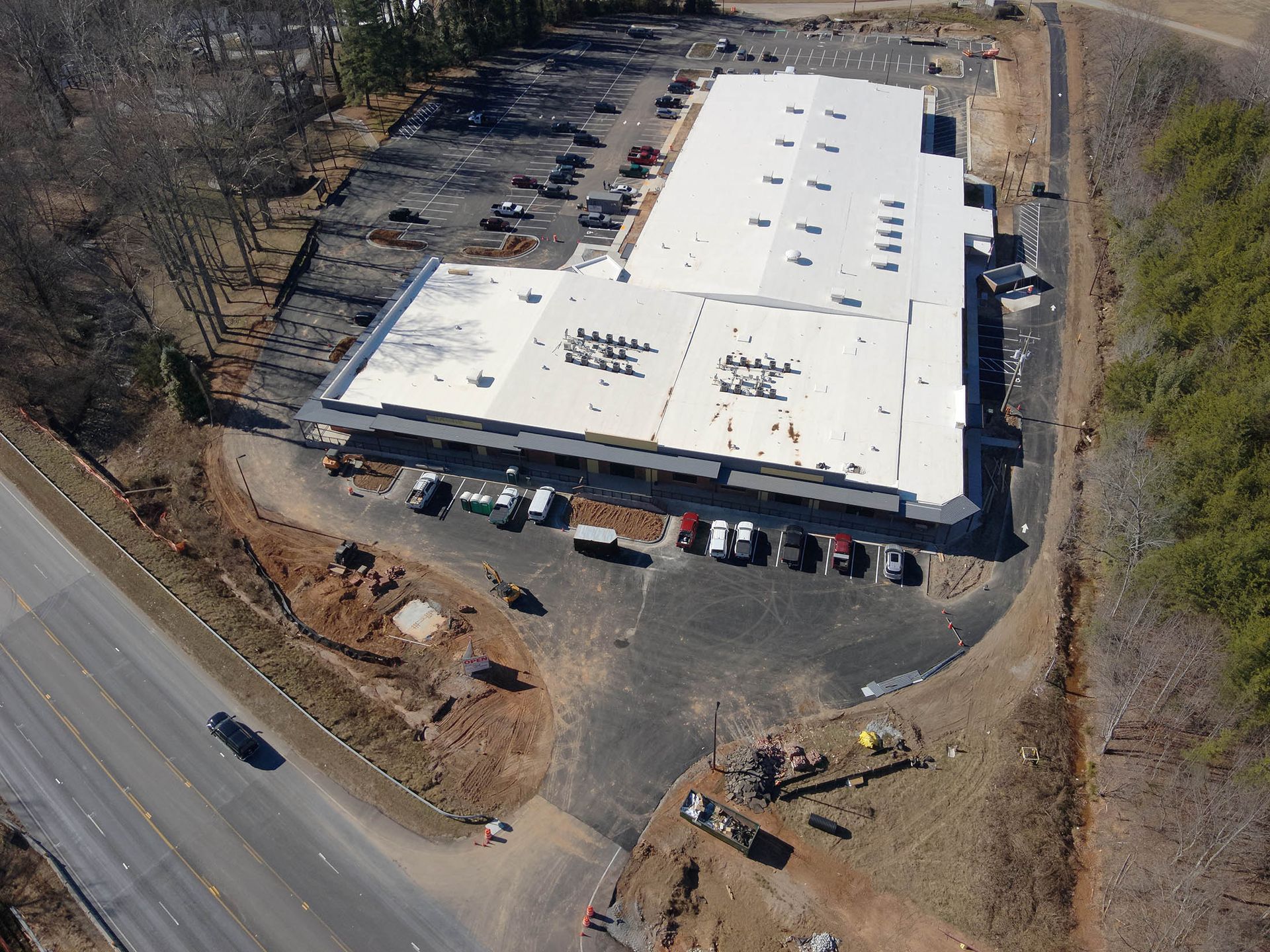 Aerial view of a large commercial building with a white roof and parking lot next to a road.