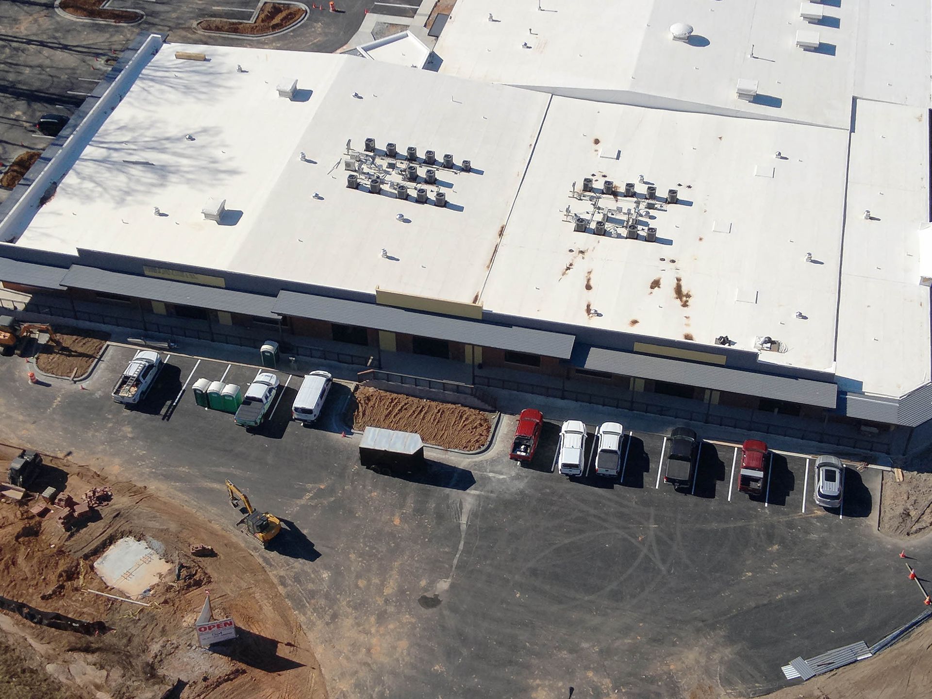 Overhead view of a commercial building with white roof, parking lot, and cars.