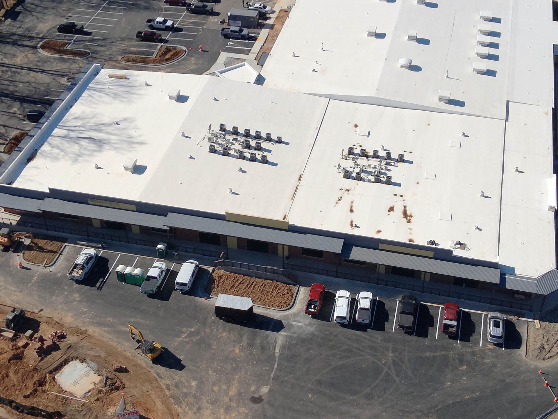 Aerial view of a commercial building with a white roof, parking lot, and parked cars.