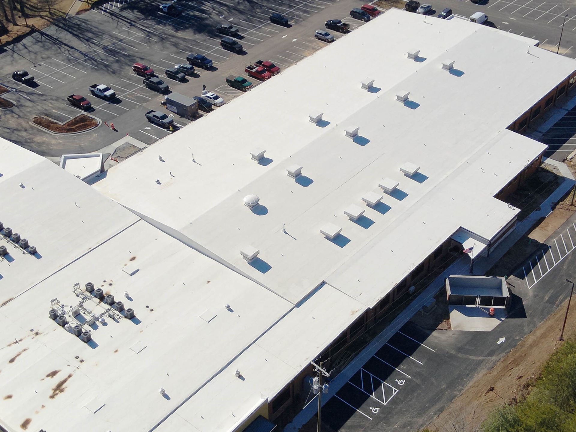 Aerial view of a white commercial building with air vents, a parking lot, and cars.