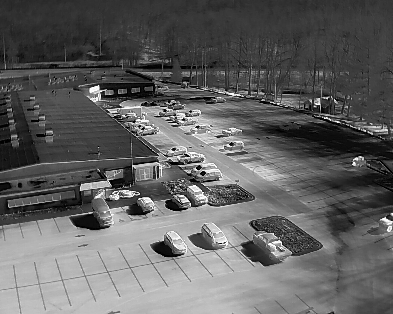 Black and white aerial view of a parking lot filled with cars in front of a building.