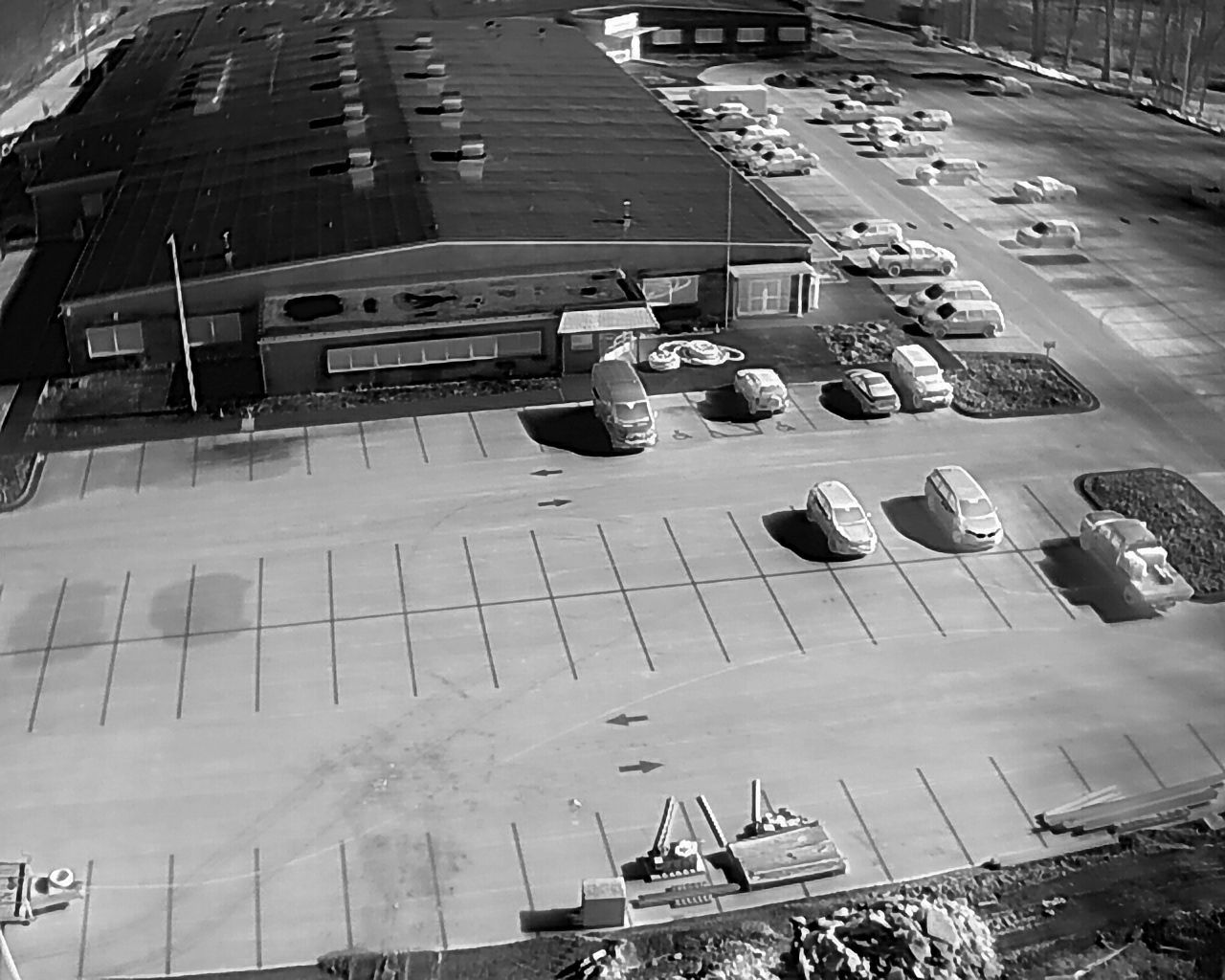Black and white overhead view of a large building with a parking lot. Cars parked in rows.