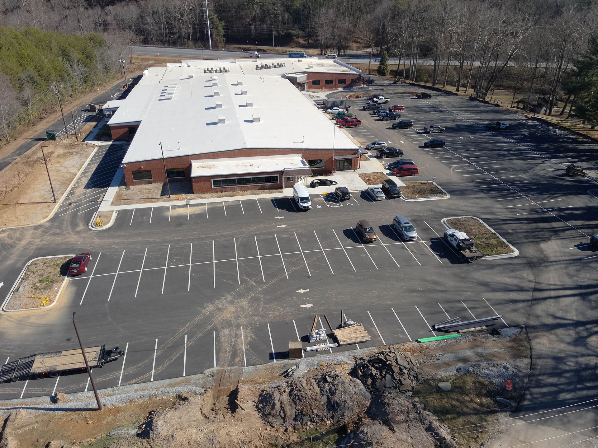 Large brick building with a long white roof and large parking lot filled with cars.