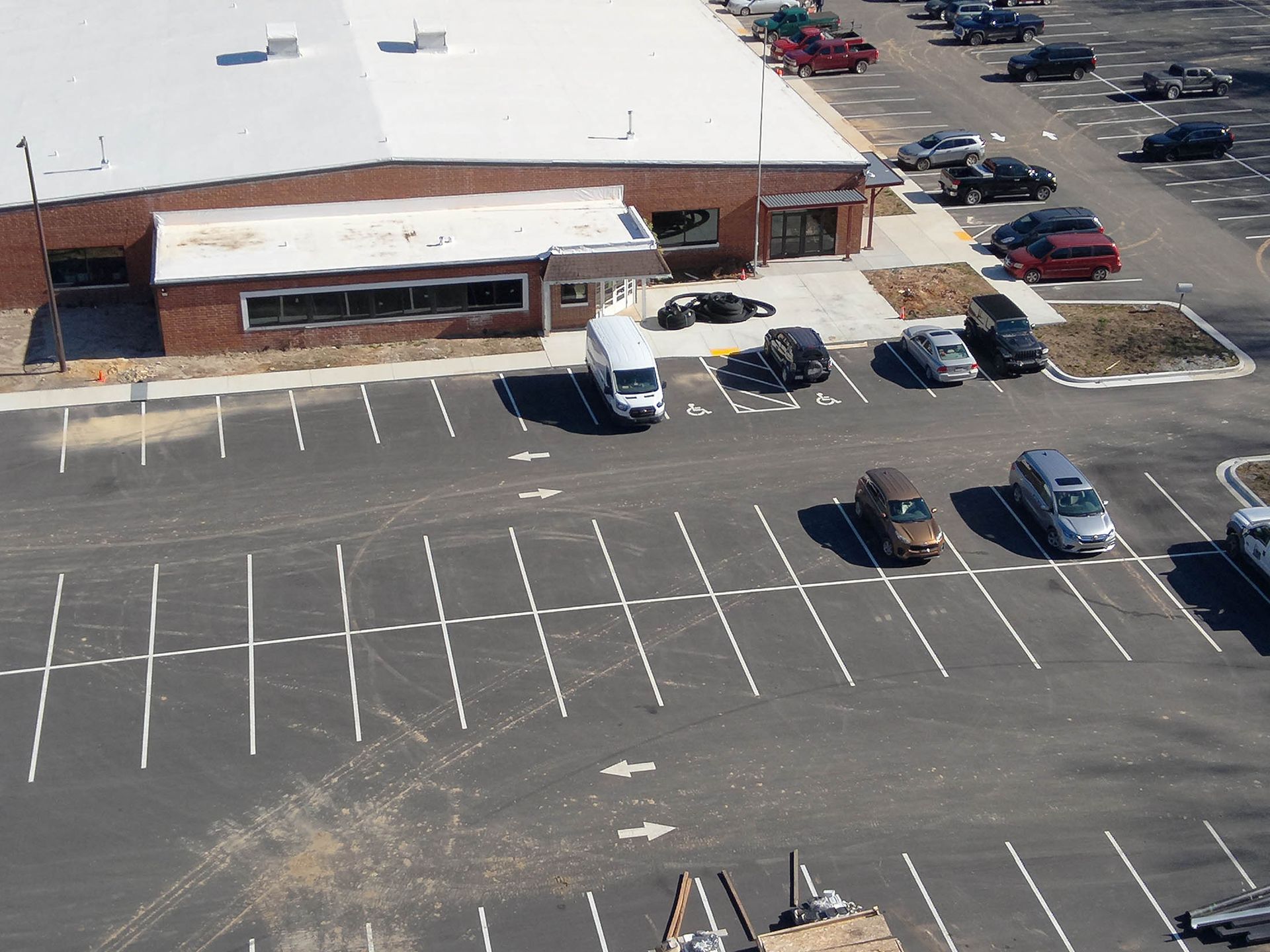 Parking lot in front of a brick building. Several cars and a white van parked, some driving.