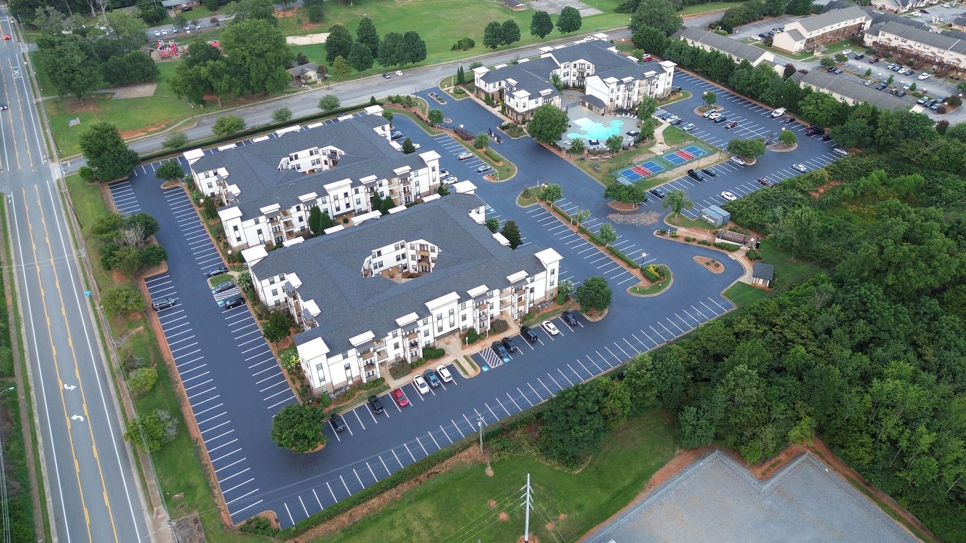 Aerial view of apartment complex with parking lots, swimming pool, and surrounding trees.